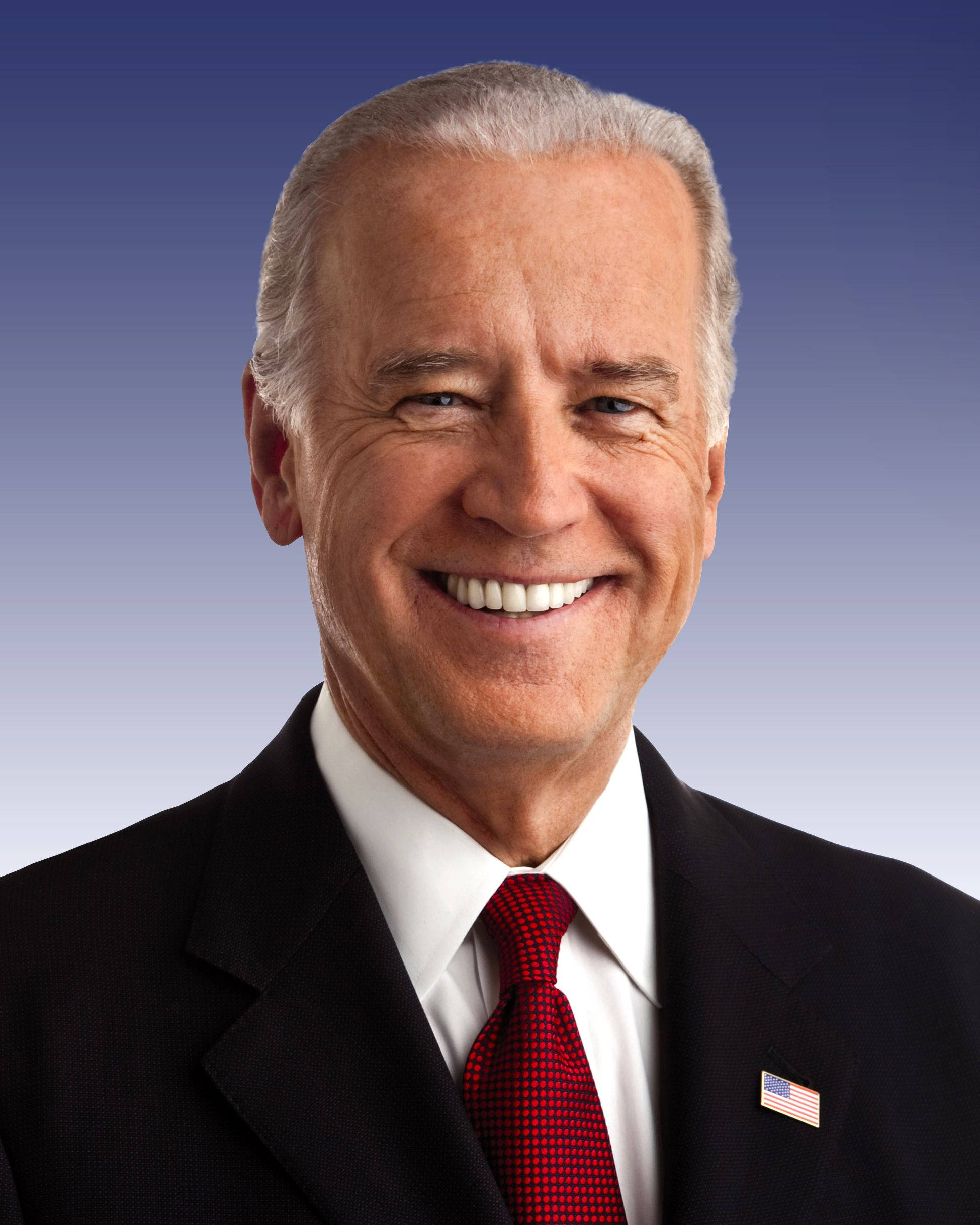 Biden 桌布 壁紙 — 一個微笑的男人穿著深色西裝和紅色領帶，站在漸變藍色背景前，翻領上別著美國國旗別針。