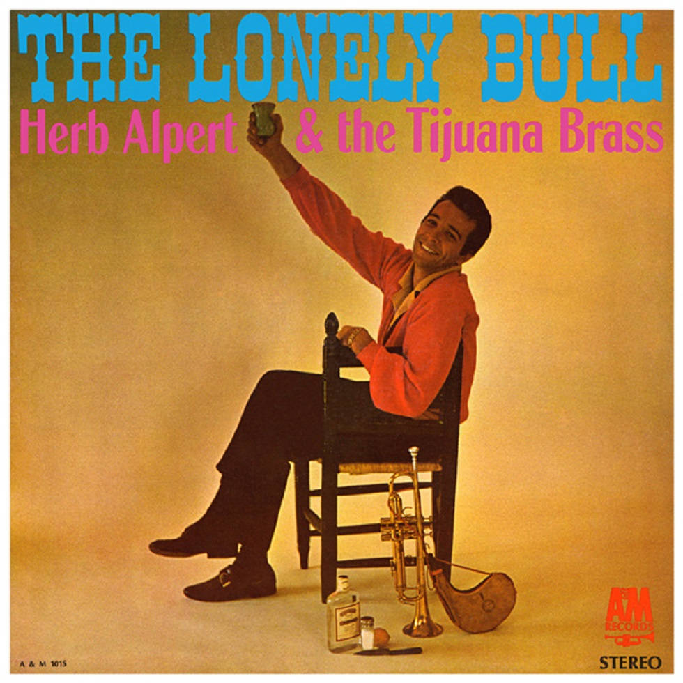 Album Cover 桌布 壁紙 — 一個微笑的男人穿著紅色外套坐在椅子上，拿著一個杯子，旁邊有喇叭和瓶子，背景是溫暖的黃色。