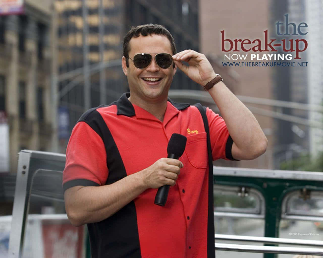 Vince Vaughn 桌布 壁紙 — 一個微笑的男人穿著紅黑相間的Polo衫，在城市的街道上拿著麥克風，同時調整他的太陽眼鏡。
