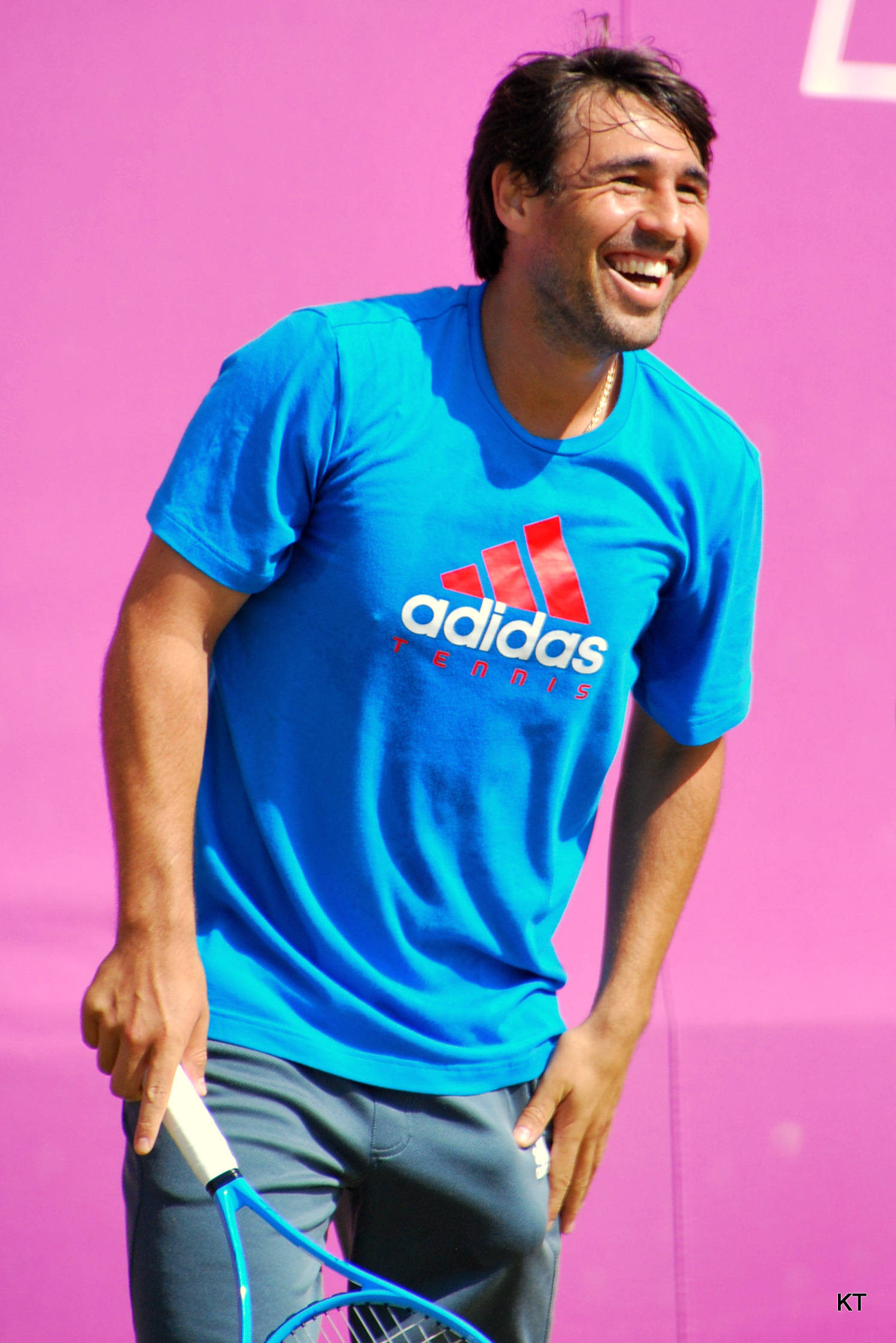 Tennis 桌布 壁紙 — 一個微笑的男人穿著藍色愛迪達網球衫，拿著網球拍對著鮮豔的粉紅色牆壁大笑。