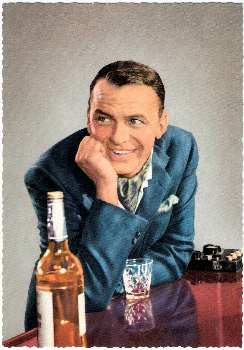 Sinatra 桌布 壁紙 — 一個微笑的男人穿著藍色西裝，靠在一張有酒瓶和琥珀色液體杯子的桌子上。