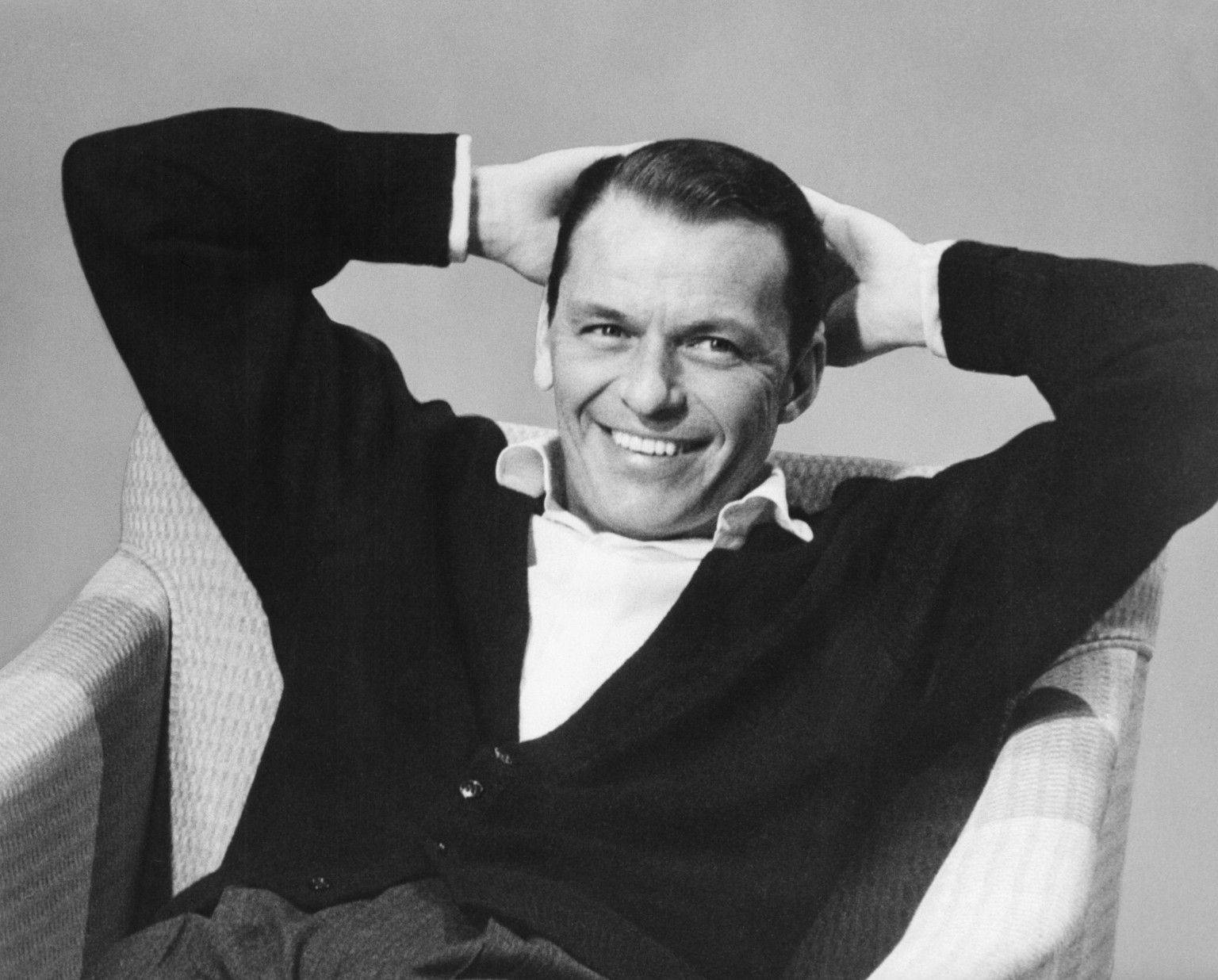 Sinatra 桌布 壁紙 — 一個微笑的男人穿著開襟毛衣，向後靠在椅子上，雙手放在腦後，經典黑白工作室肖像。
