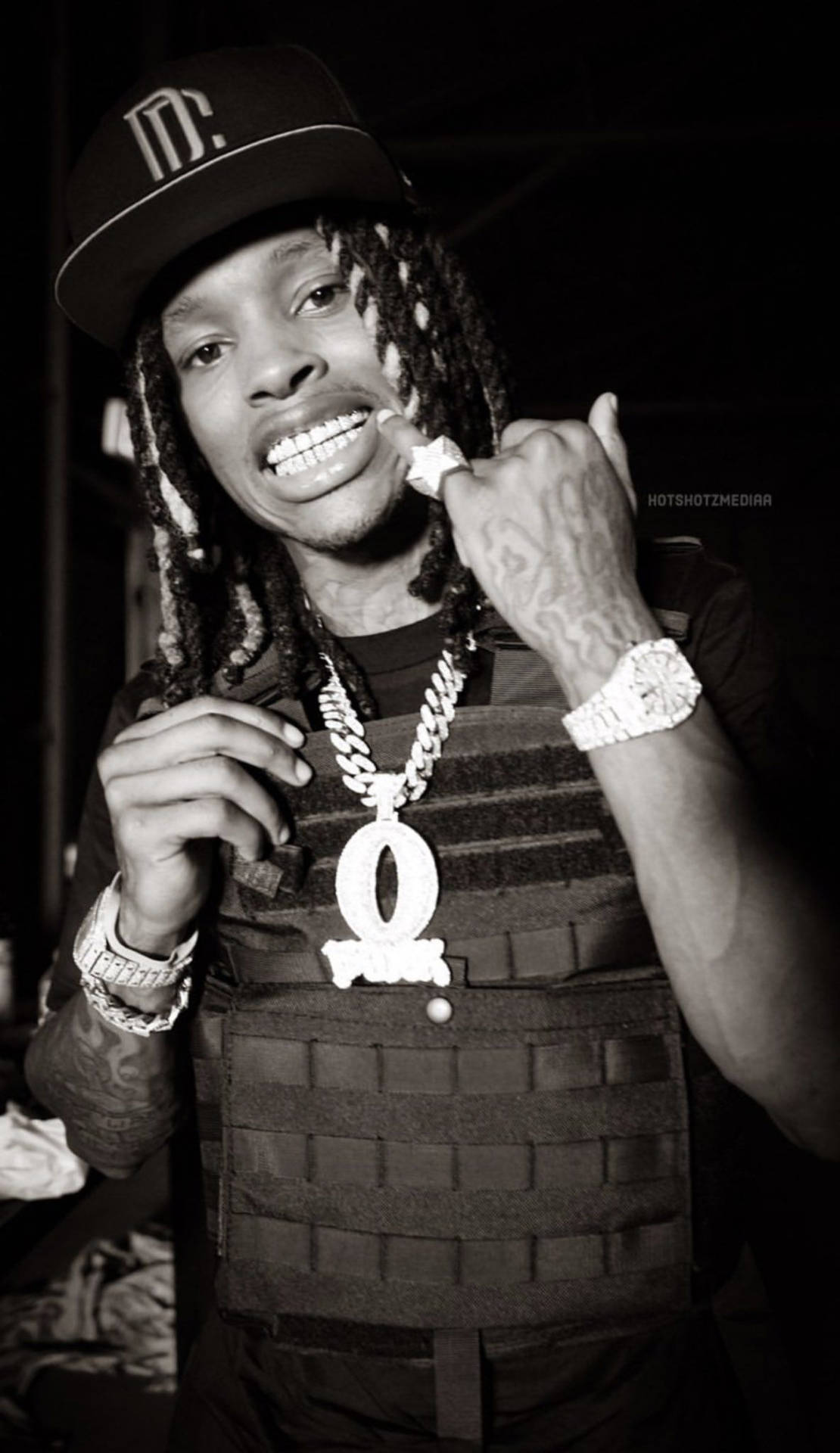 留著辮子頭、穿著戰術背心和珠寶的男士對著鏡頭微笑。 — King Von 壁紙