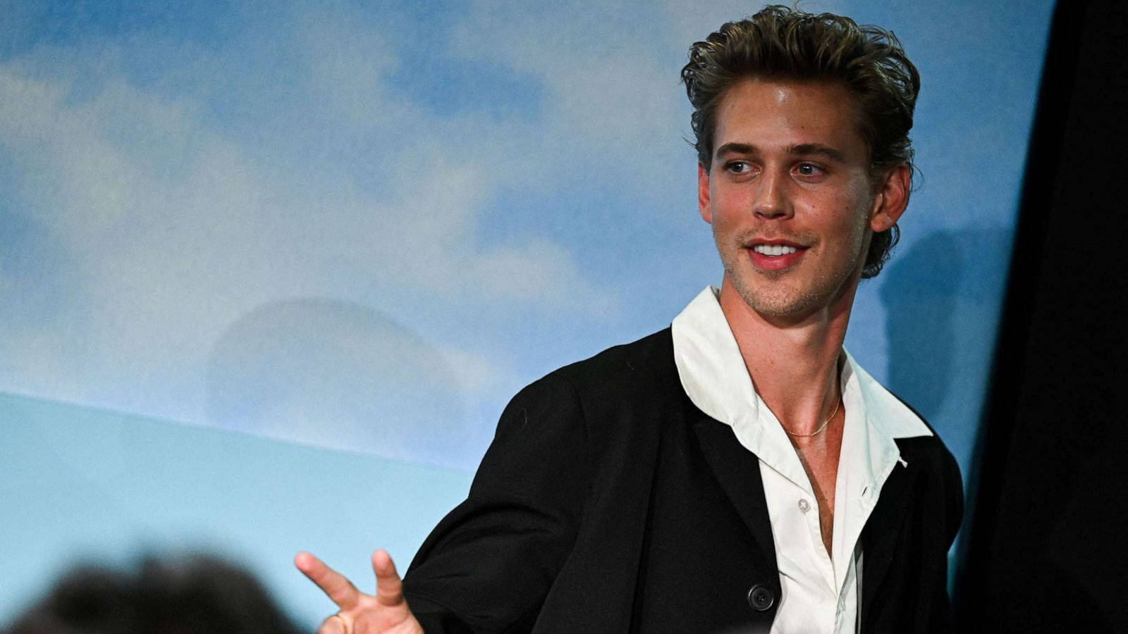 Celebrity 桌布 壁紙 — 一個微笑的男子，頭髮造型時尚，穿著黑色西裝外套內搭白襯衫，背景是藍天。
