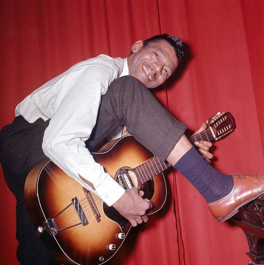 Little Walter 桌布 壁紙 — 一個微笑的白襯衫男人靠著紅色窗簾，手持一把旭日紋木吉他。