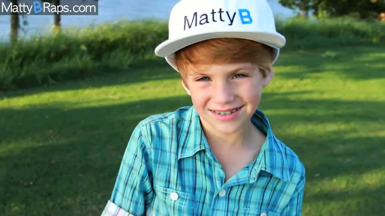 Matty B 桌布 壁紙 — 一個微笑的紅髮男孩戴著白色帽子，穿著藍色格子衫，在戶外的草地上。