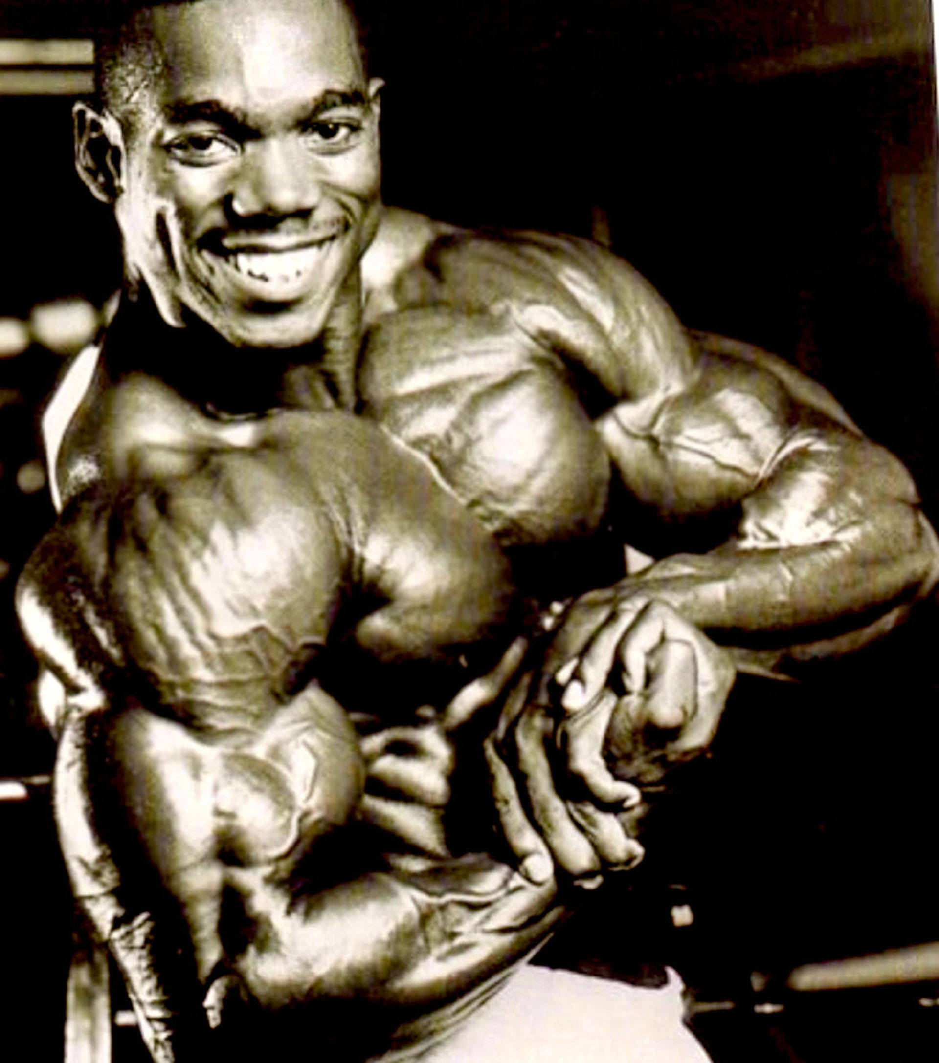 flex wheeler 桌布 壁紙 — 一個微笑的肌肉男在戲劇性的黑白照片中展示他清晰的體格。