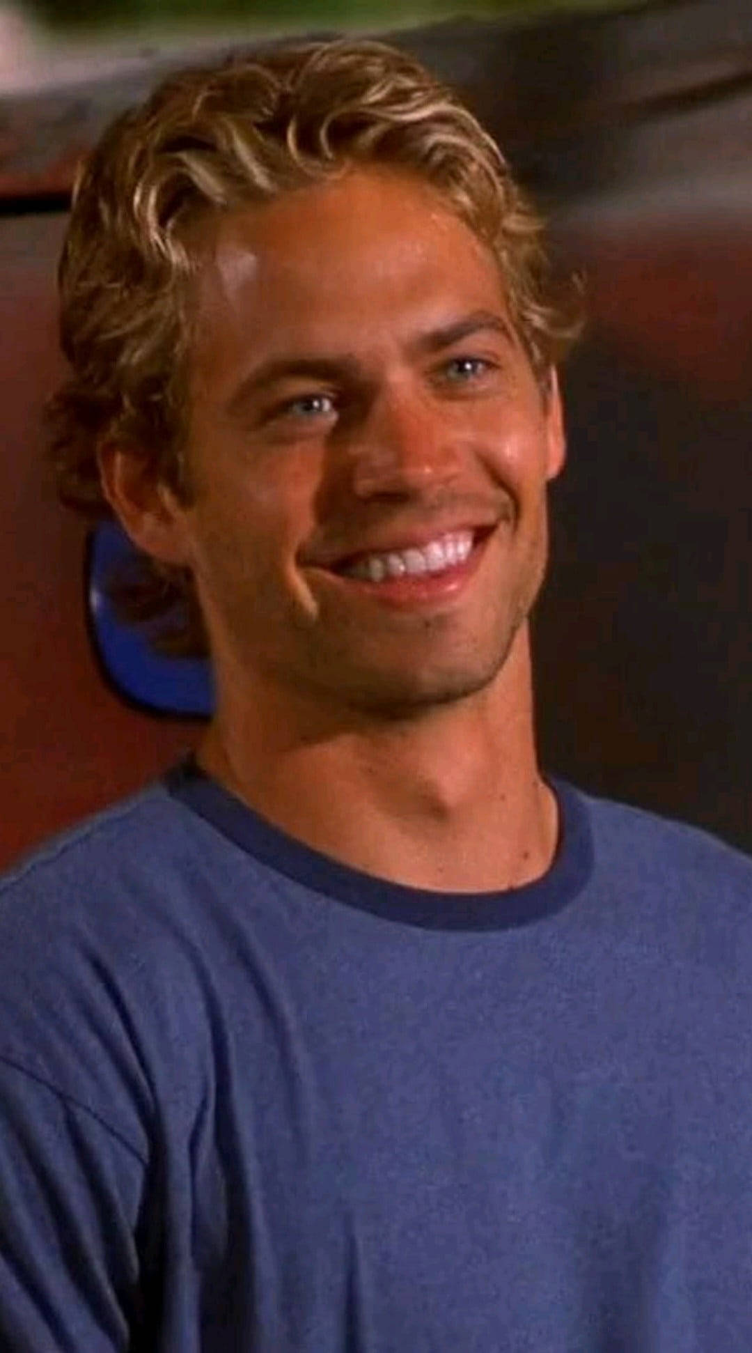 Paul Walker 桌布 壁紙 — 一個微笑的金髮捲髮男子穿著藍色T恤的特寫。