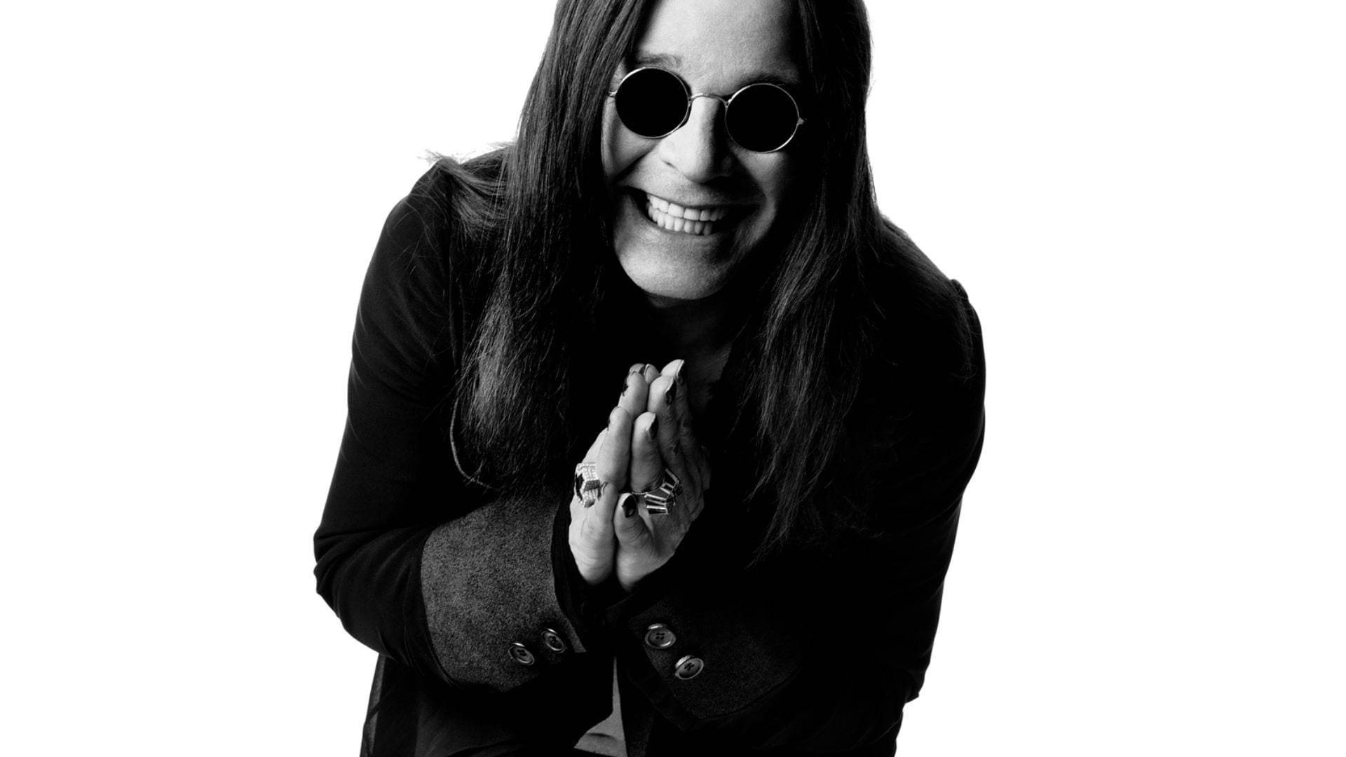 Ozzy Osbourne 桌布 壁紙 — 一個微笑的長髮男子戴著圓形太陽眼鏡，雙手合攏的黑白肖像。