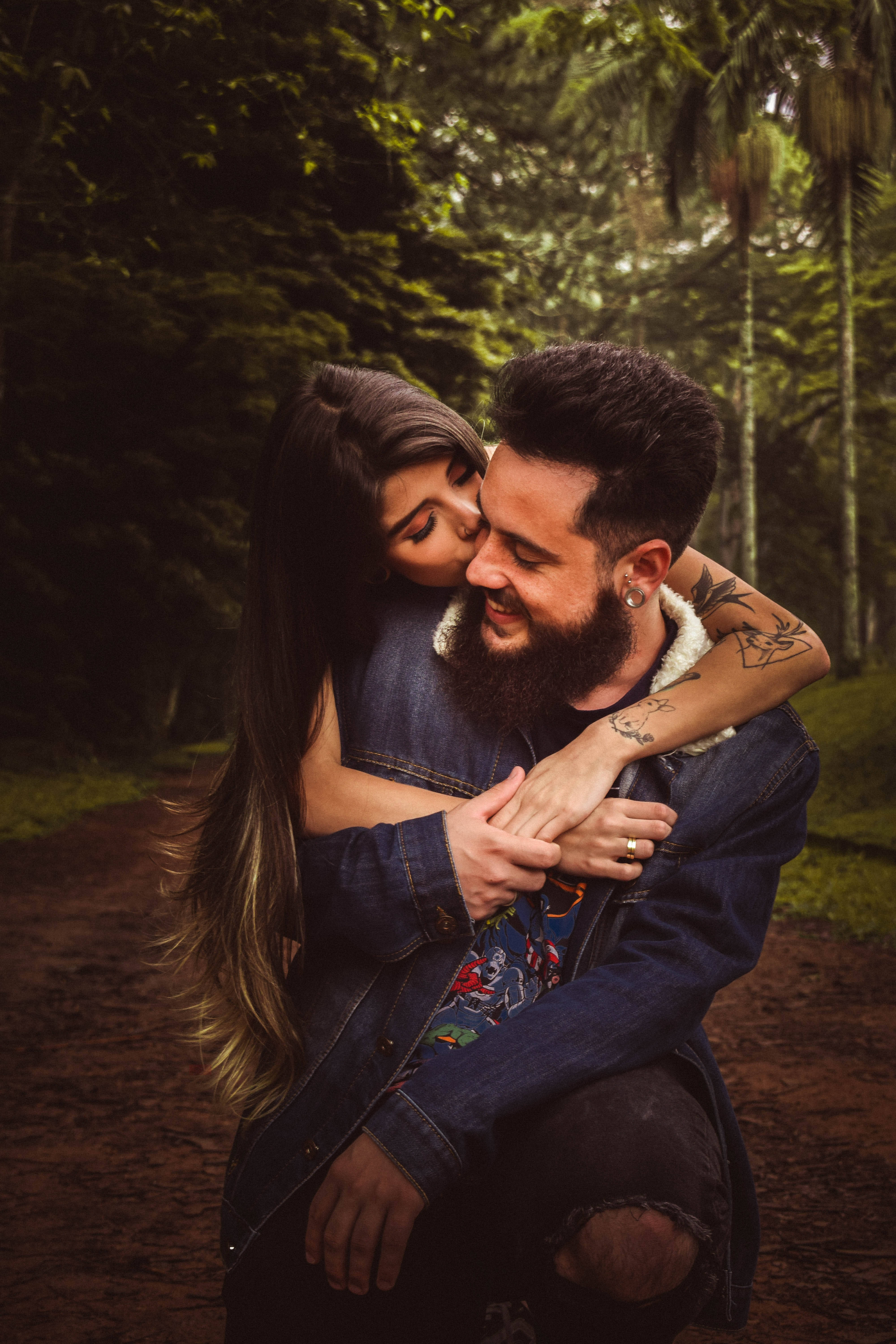 Romance 桌布 壁紙 — 一個微笑的鬍鬚男和女人在森林小徑上溫暖地擁抱，周圍是茂密的綠樹。