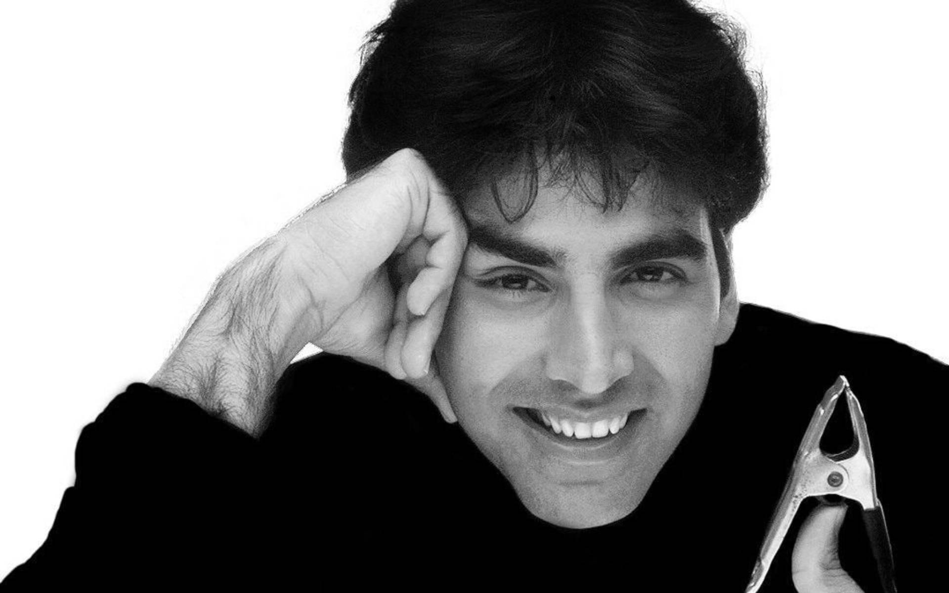 Akshay Kumar 桌布 壁紙 — 一個微笑的黑白男人拿著夾子，將頭靠在手上，背景是純白色。