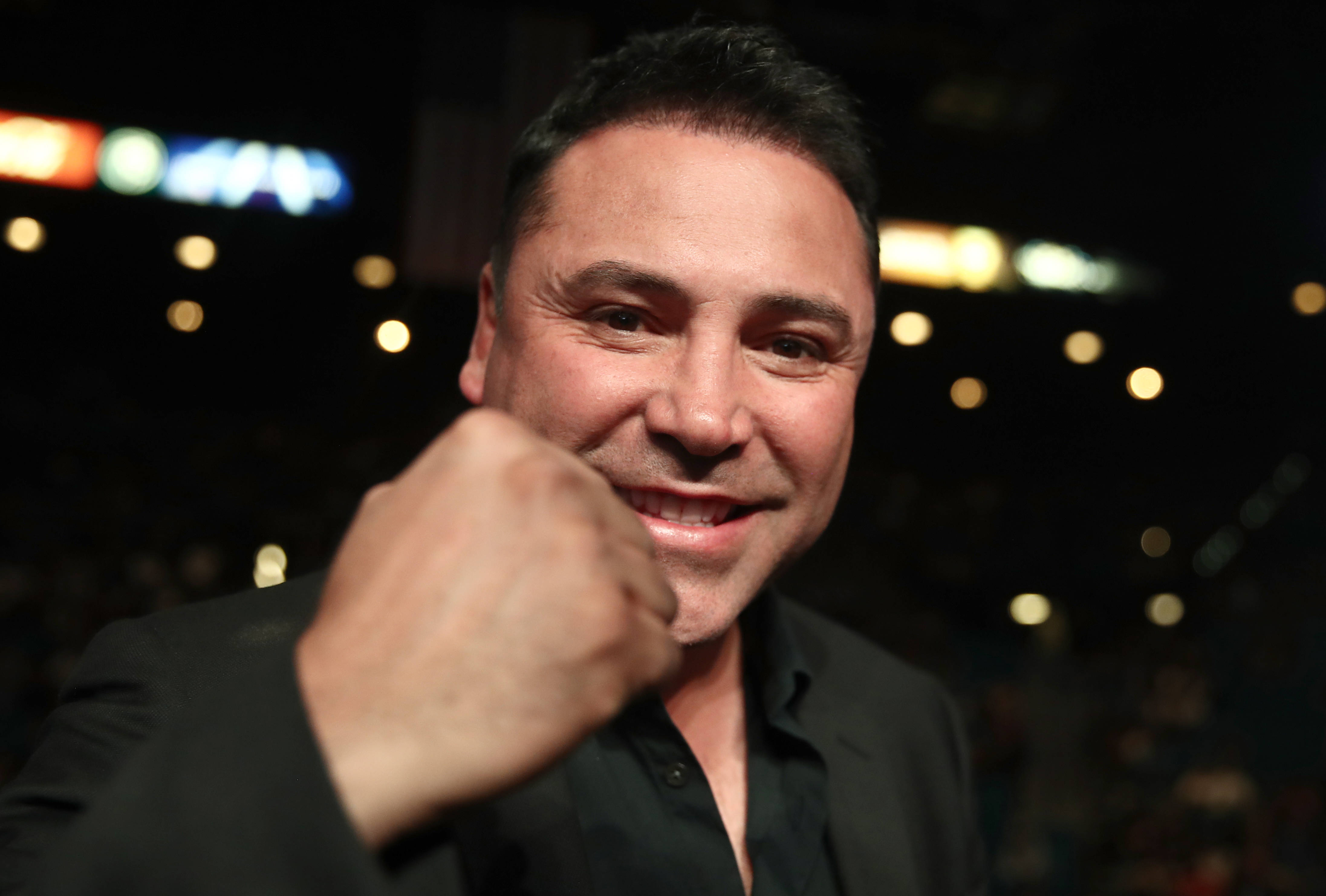 Boxing 桌布 壁紙 — 一個微笑的黑西裝男子，在模糊的體育場背景下，向鏡頭做出俏皮的拳頭碰撞動作。