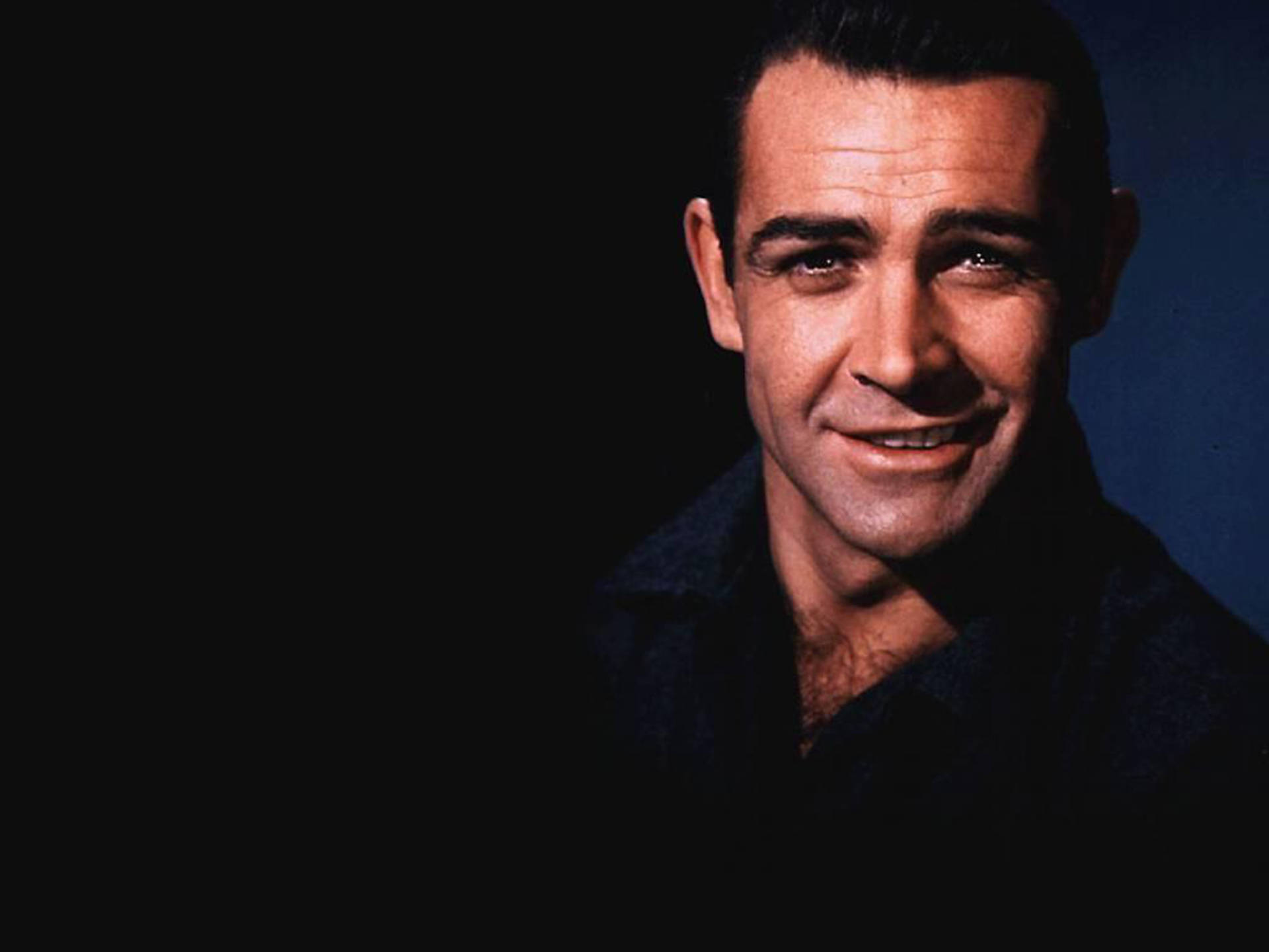 Sean Connery 桌布 壁紙 — 一個微笑的黑髮男子在藍色燈光的黑暗背景下的特寫肖像。