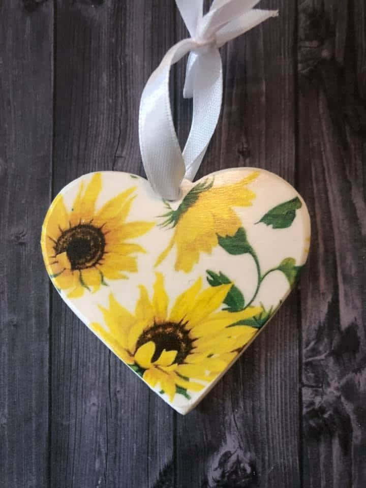 Beautiful Sunflower 桌布 壁紙 — 一個心形木製裝飾品，繪有鮮豔的向日葵，用白色絲帶掛在深色風化的木頭上。