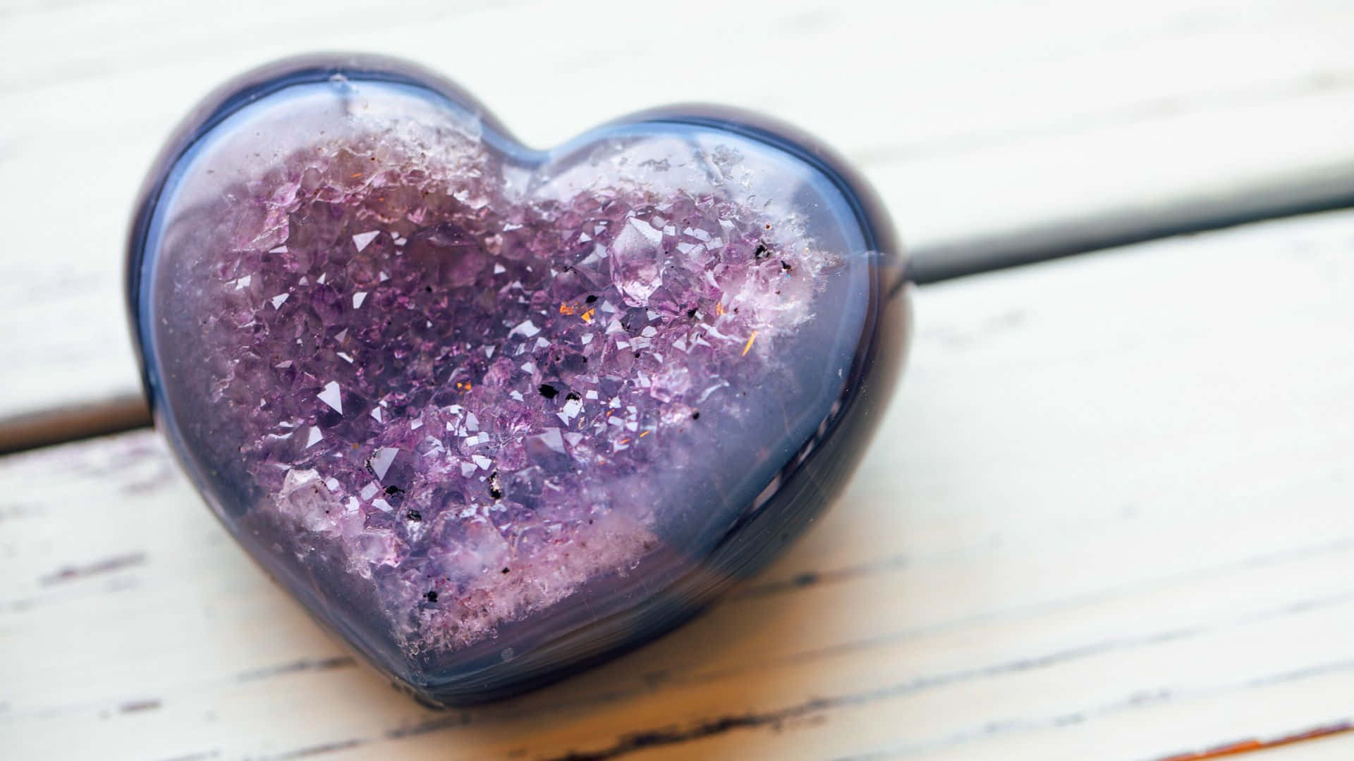 Heart 桌布 壁紙 — 一個心形玻璃容器裝滿閃閃發光的紫色紫水晶晶體，放置在經風化的白色木質表面上。