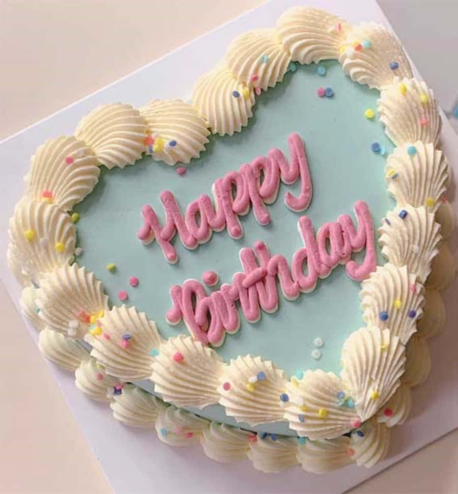 Happy Birthday Cake 桌布 壁紙 — 一個心形生日蛋糕，帶有淺藍色糖霜和粉紅色擠花文字，周圍環繞著白色貝殼邊緣和彩色糖粒。