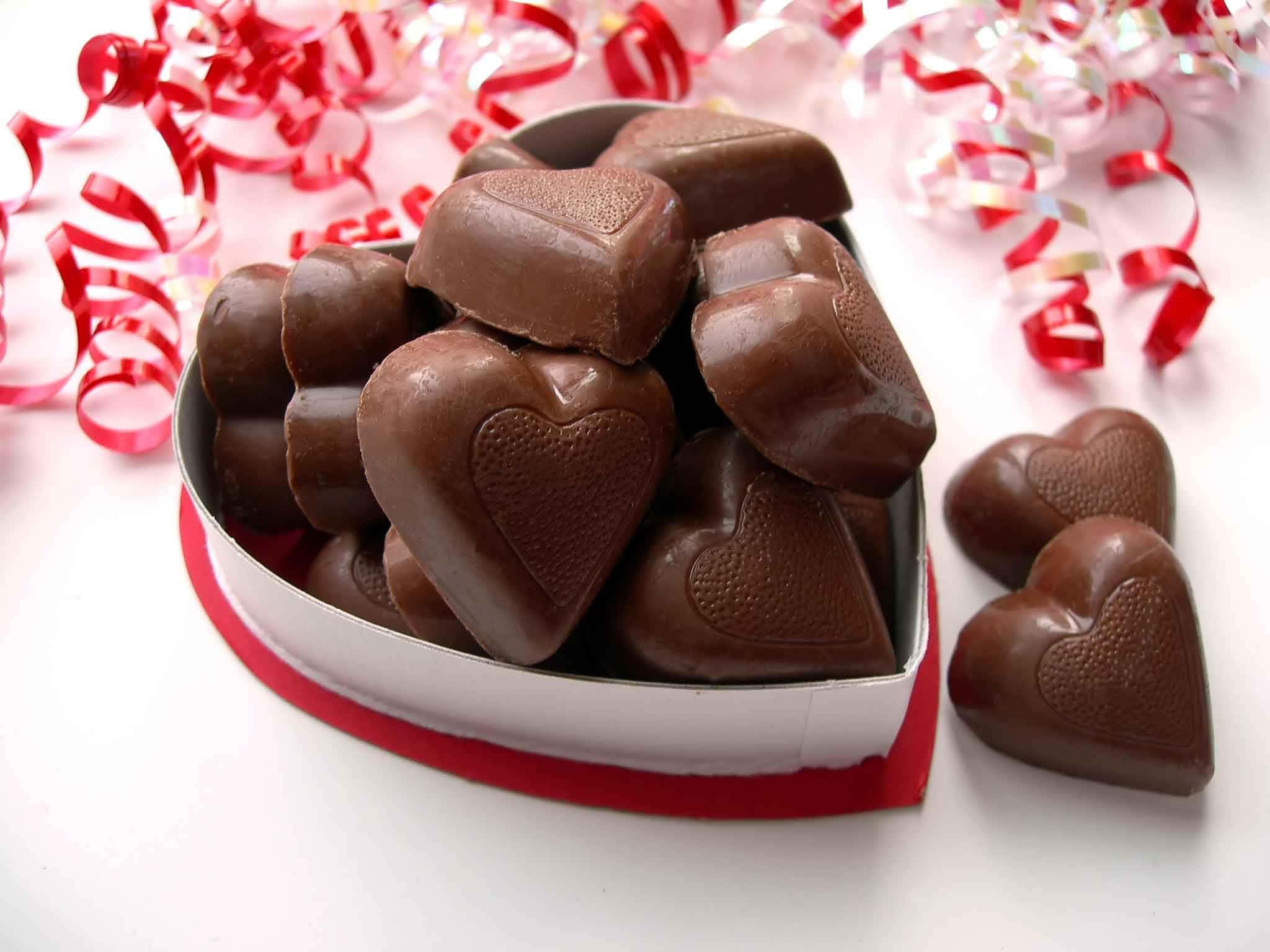 Chocolate 桌布 壁紙 — 一個心形盒子，裝滿了閃亮的黑巧克力心形，周圍是紅色紙屑。