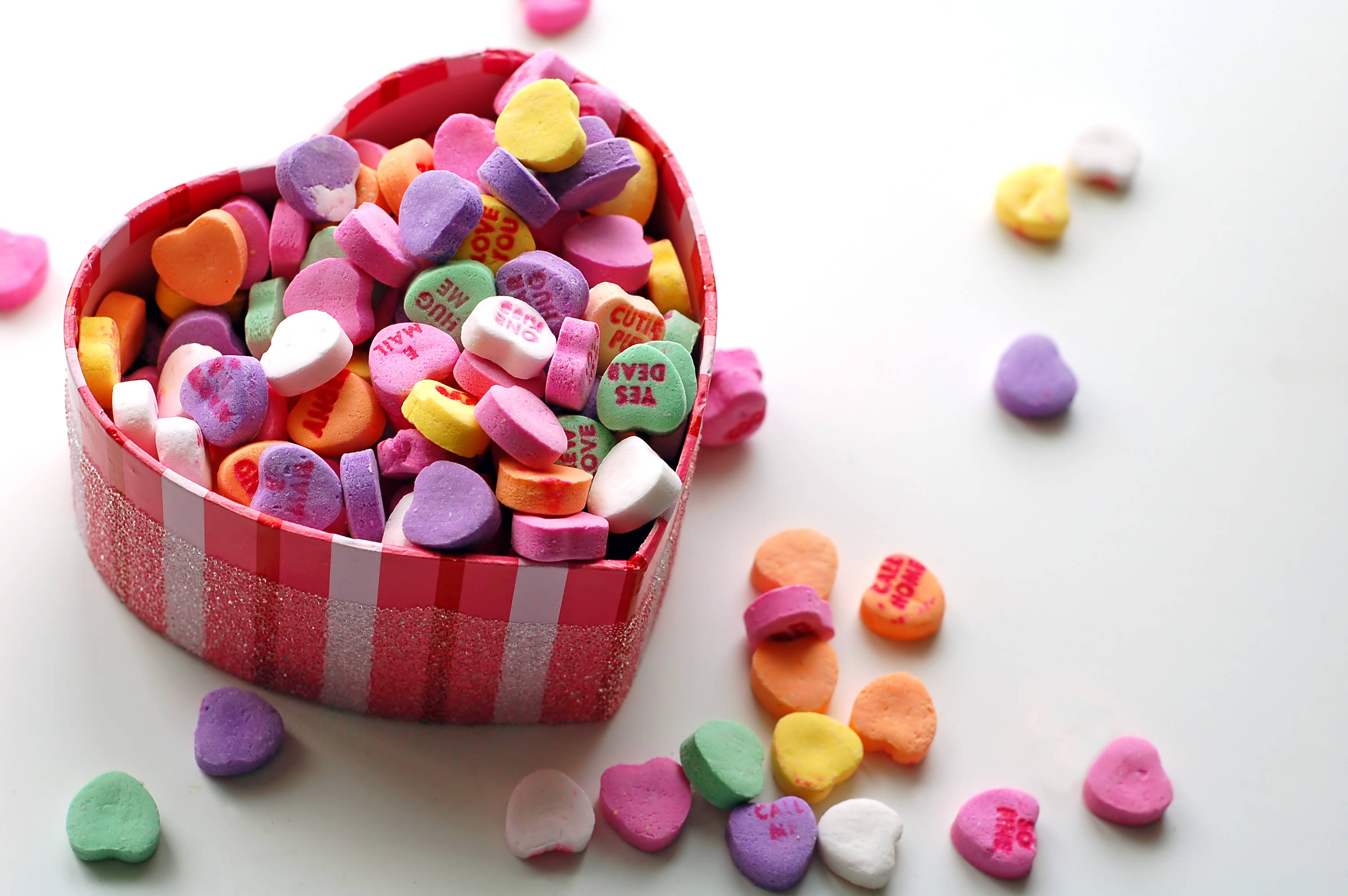Tumblr Valentines Day 桌布 壁紙 — 一個心形盒子裝滿色彩繽紛的心形糖果，溢出到白色表面上。