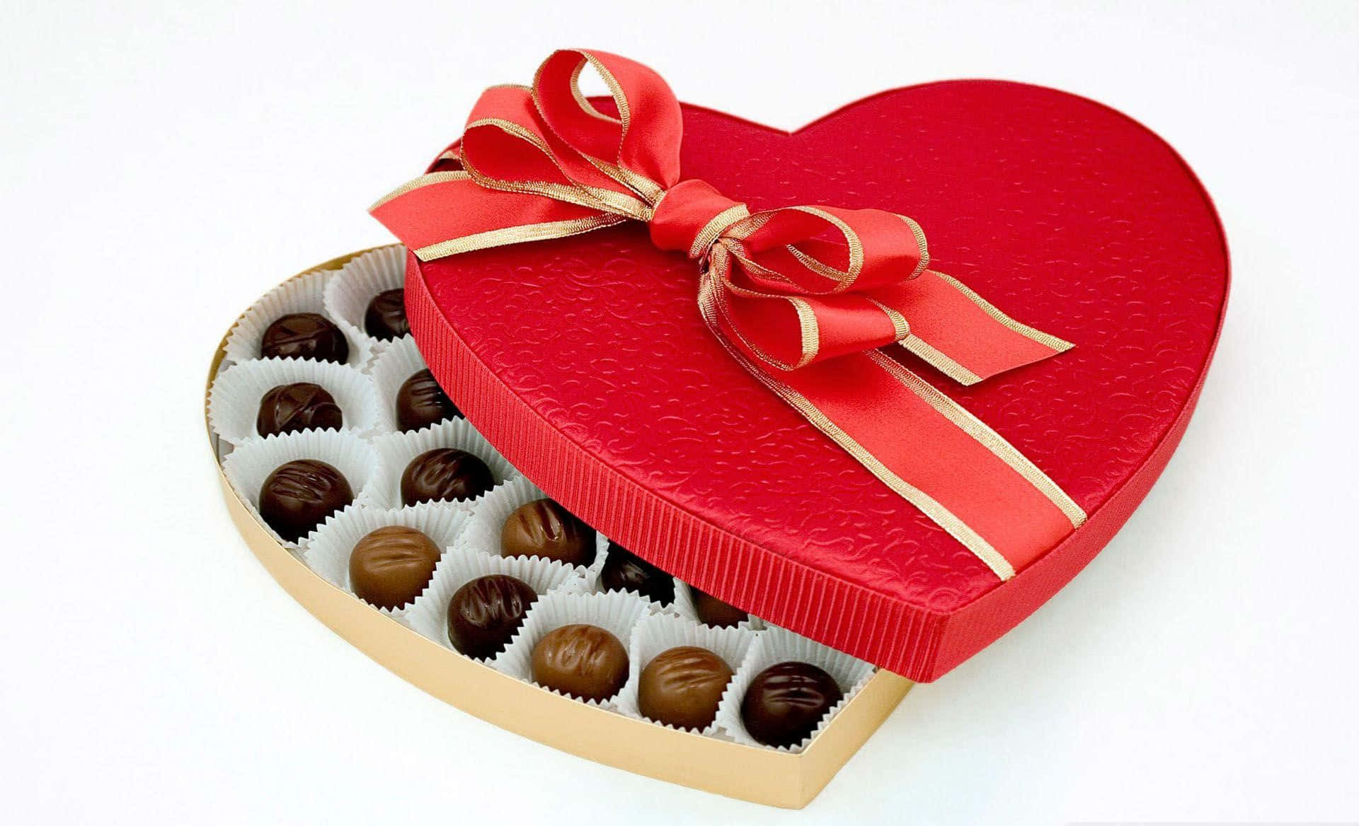 Chocolate 桌布 壁紙 — 一個心形紅色巧克力盒，配有金色絲帶蝴蝶結，展示出白色紙杯中的各種黑巧克力和牛奶巧克力。