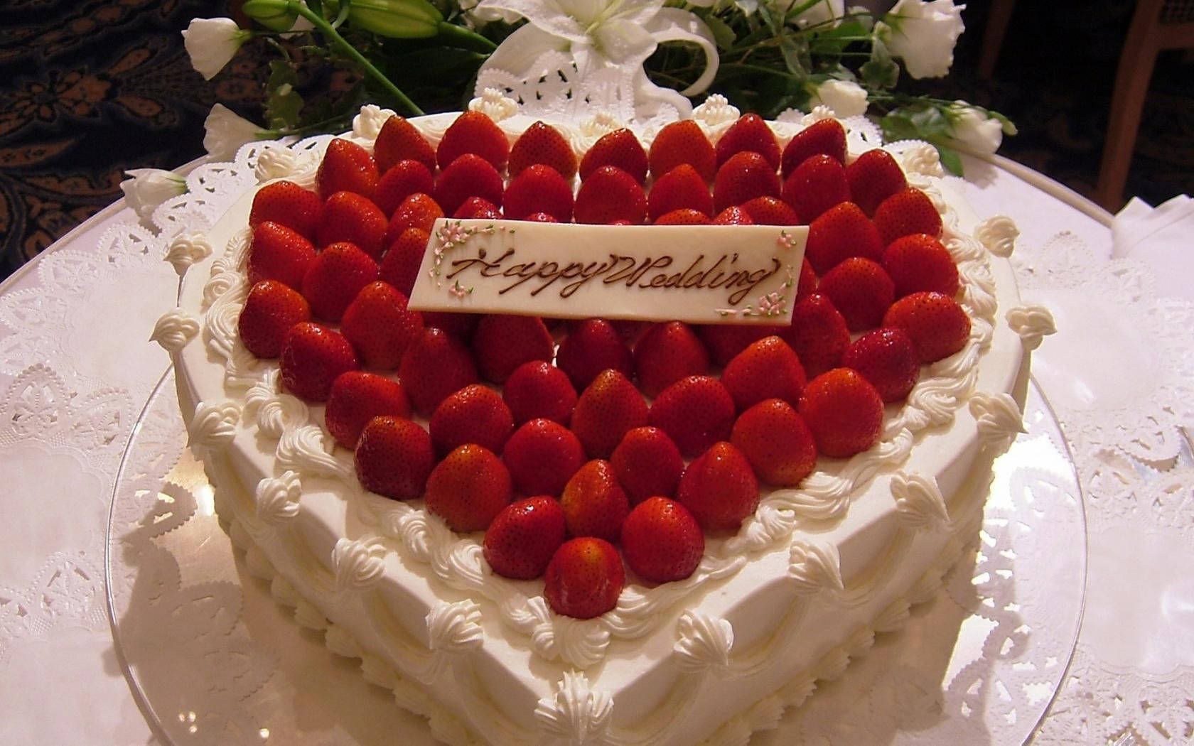Birthday Cake 桌布 壁紙 — 一個心形結婚蛋糕，飾以新鮮草莓和「Happy Wedding」牌匾，優雅地放在蕾絲桌布上。
