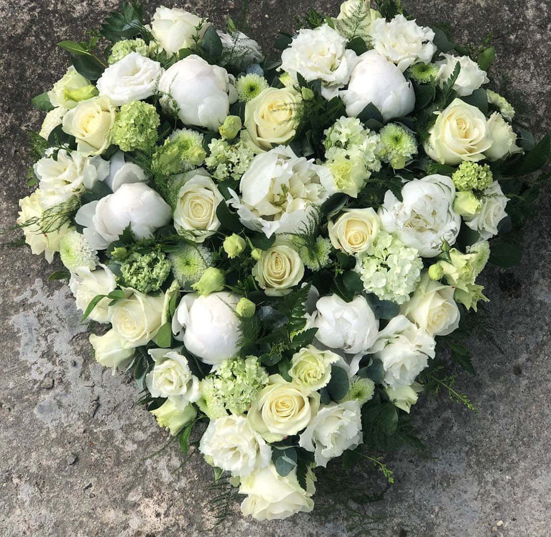 Funeral Flower Arrangements 桌布 壁紙 — 一個心形花卉佈置，由白玫瑰、牡丹和綠色繡球花組成，放置在灰色石面上。