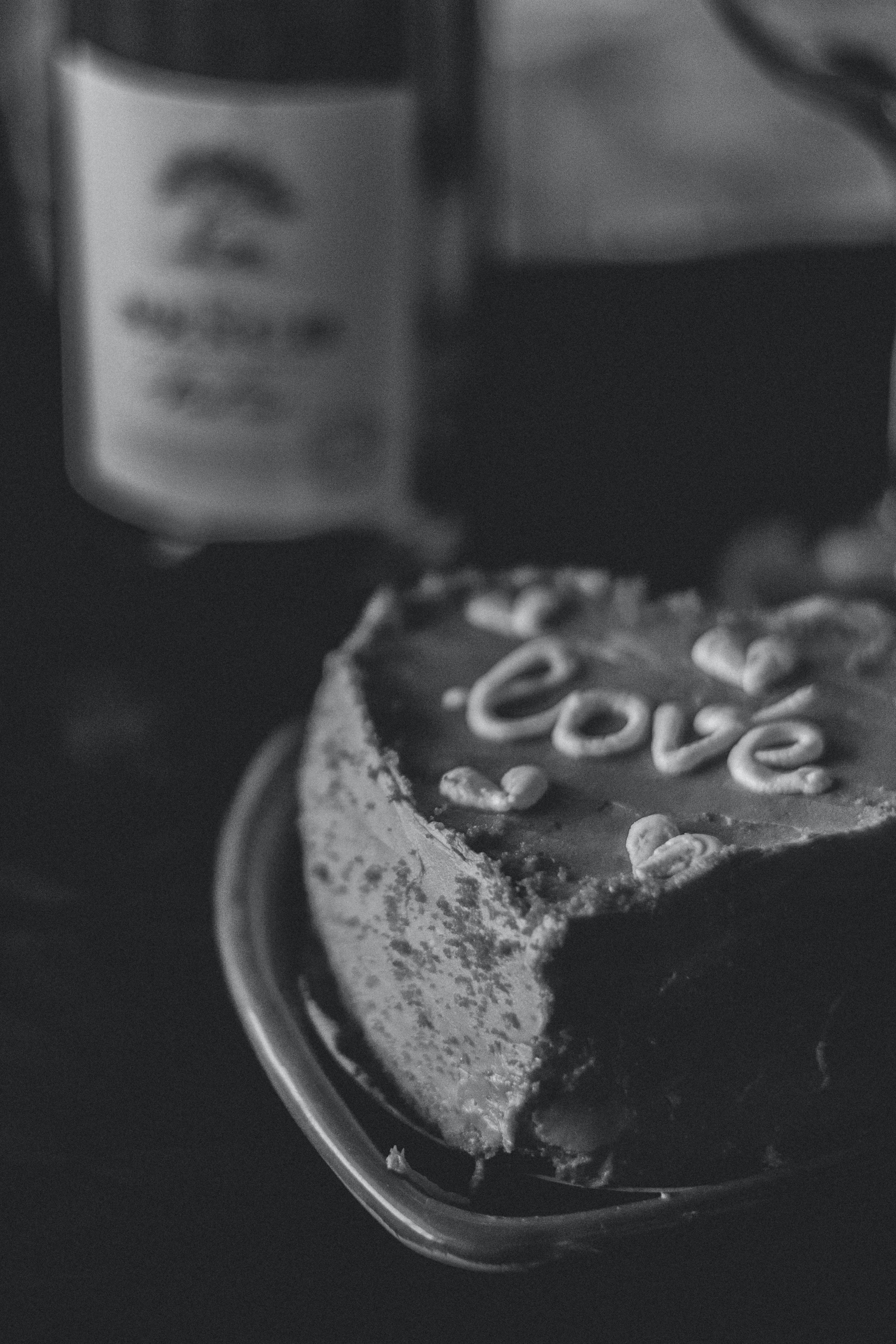 愛心 桌布 壁紙 — 一個心形蛋糕的黑白特寫，上面用糖霜寫著「love」，旁邊有一個模糊的瓶子和散落的心形。