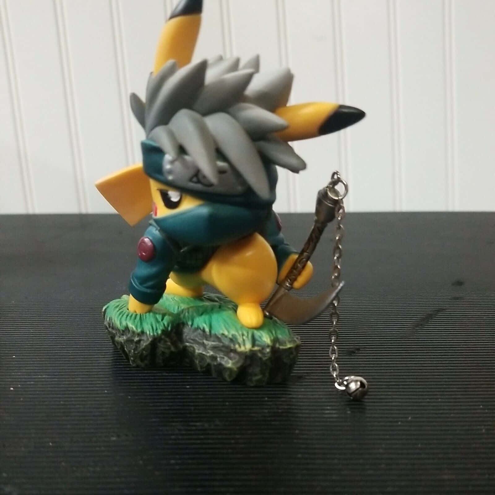 Pokemon Figures 桌布 壁紙 — 一個忍者主題的皮卡丘公仔，灰色尖刺頭髮和藍色面具，站在岩石底座上，手持鏈條武器。