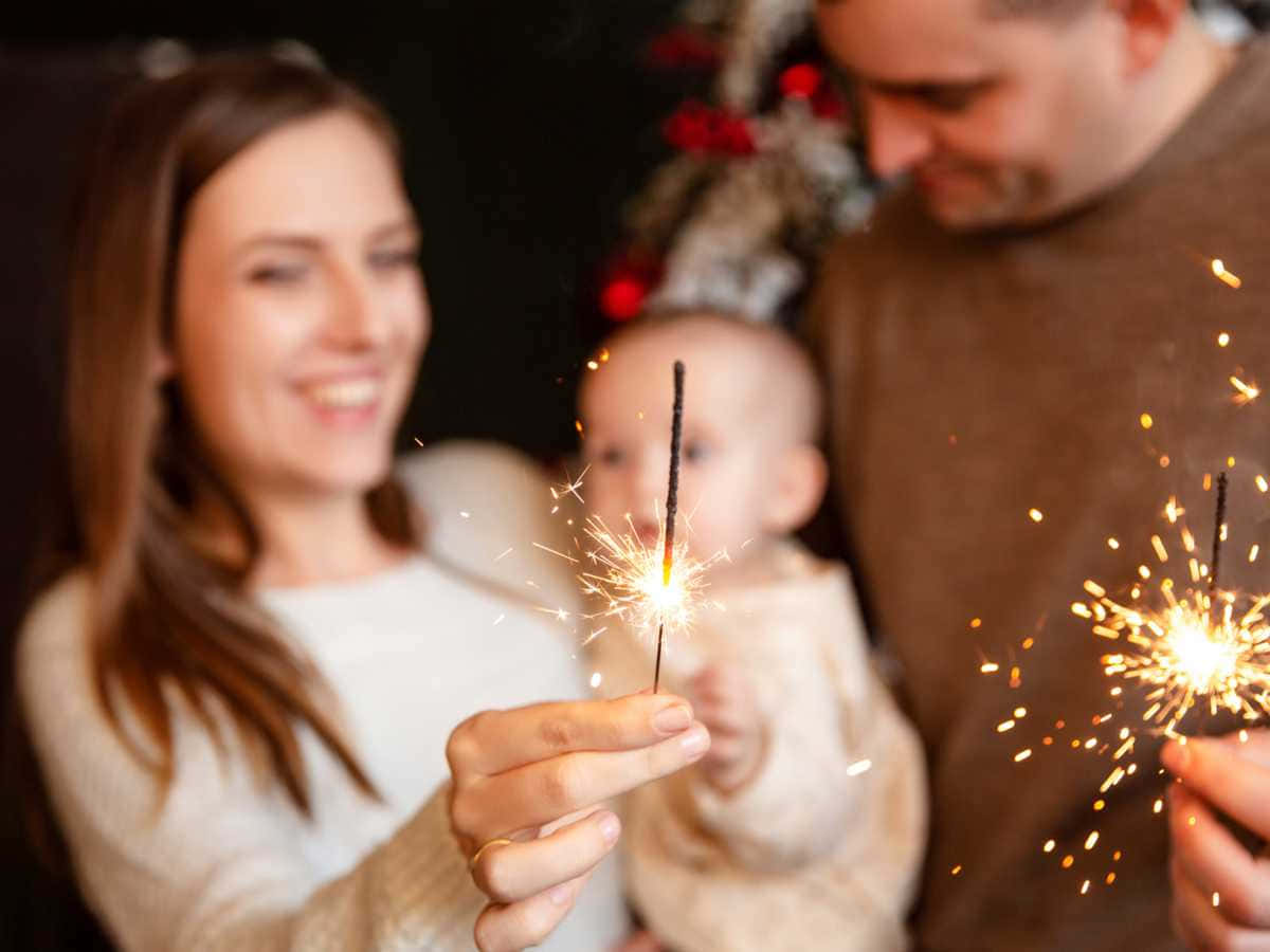 New Years Eve 桌布 壁紙 — 一個快樂的三口之家在室內手持閃閃發光的煙火，背景是裝飾好的聖誕樹。