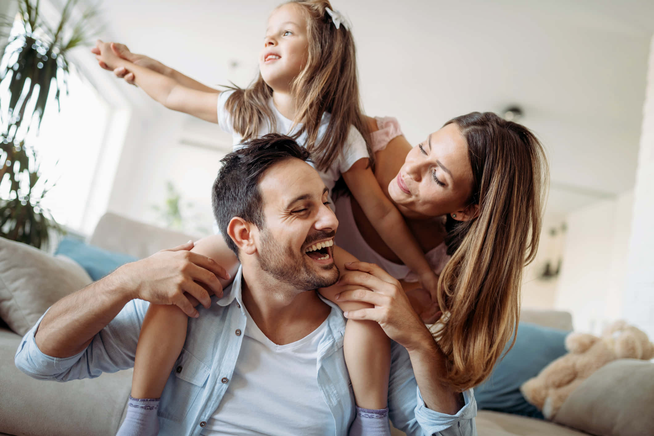 Family 桌布 壁紙 — 一個快樂的三口之家在明亮的客廳裡一起大笑，自然光線充足，家具舒適。