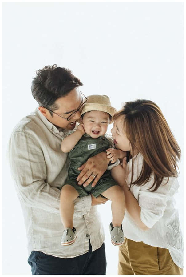 Family Portrait 桌布 壁紙 — 一個快樂的三口之家在明亮的白色背景和柔和自然光線下分享溫馨時刻。