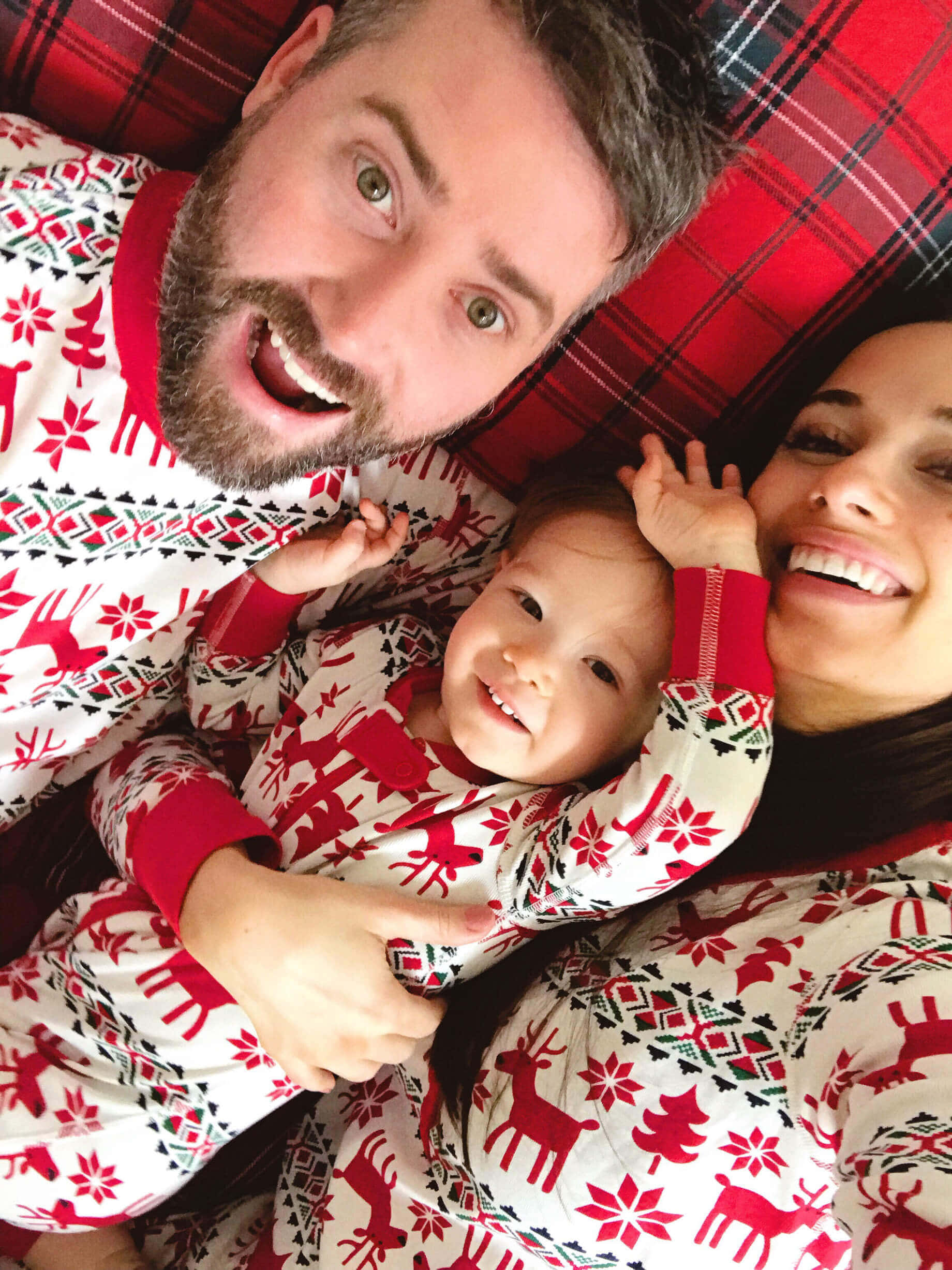 Family 桌布 壁紙 — 一個快樂的三口之家穿著相配的紅白節日睡衣，在格子沙發上緊密地微笑。