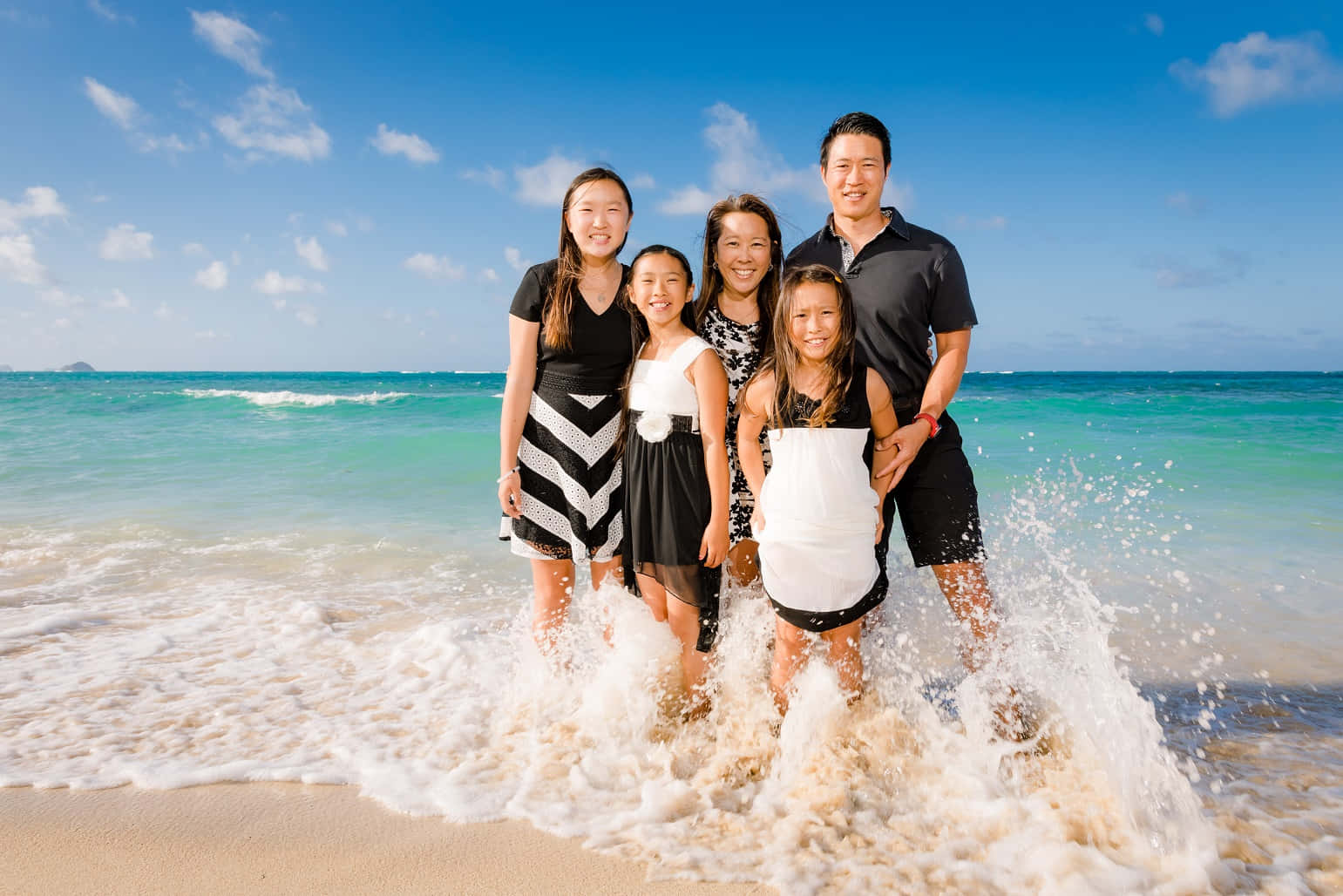 Beach Family 桌布 壁紙 — 一個快樂的五口之家站在淺海水中，海浪在他們腳邊飛濺，頭頂是明亮的藍天。