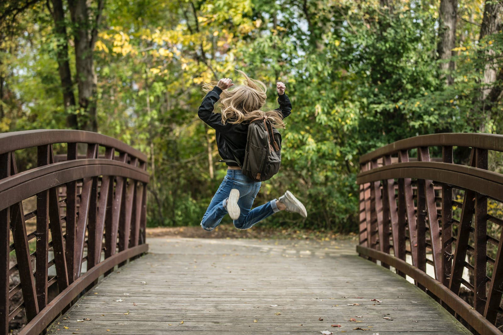 Jumping 桌布 壁紙 — 一個快樂的人在木橋上跳躍，四周環繞著秋天的樹葉。