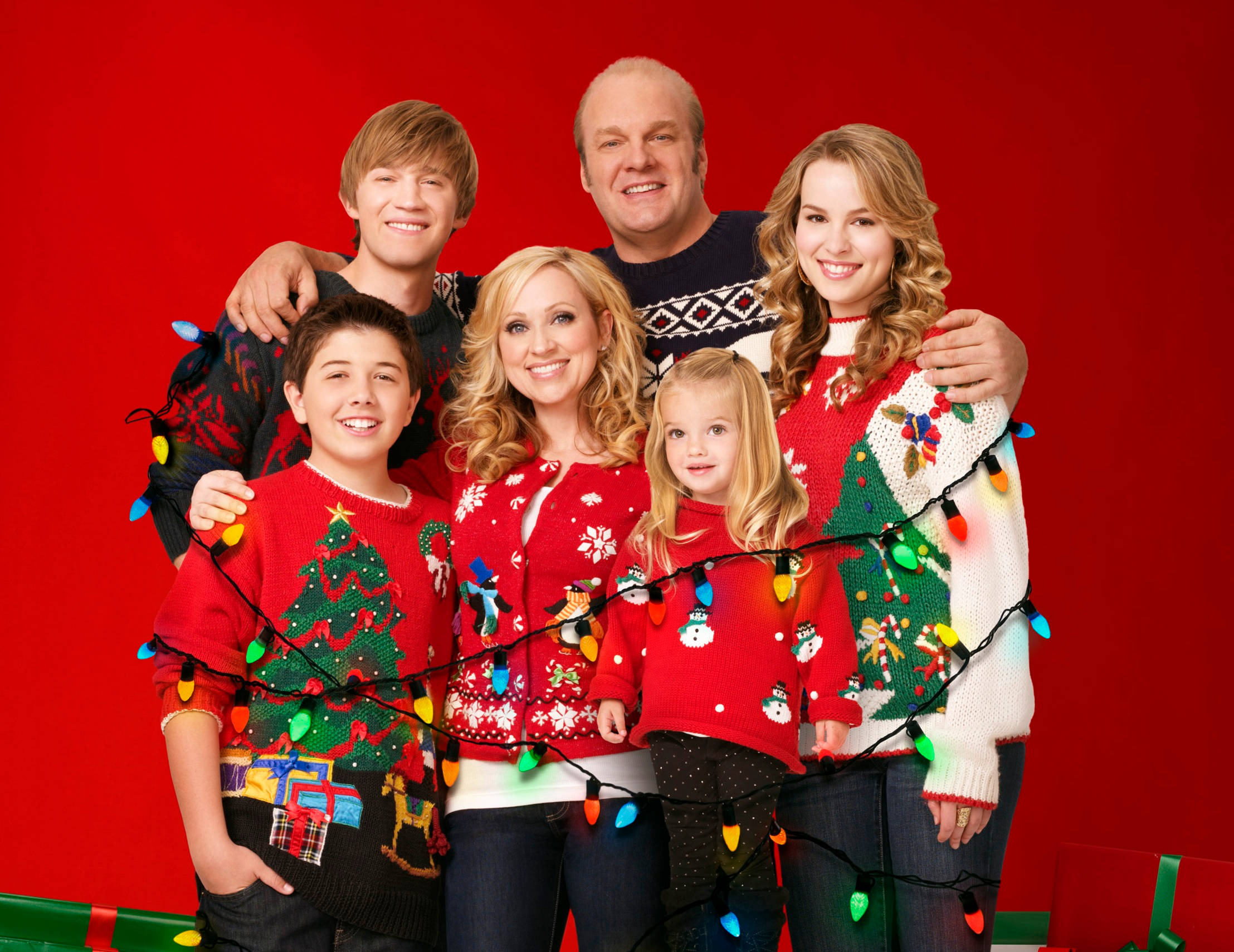 Good Luck Charlie 桌布 壁紙 — 一個快樂的六人家庭一起擺姿勢，穿著節日聖誕毛衣，裝飾著聖誕燈，背景是鮮豔的紅色。