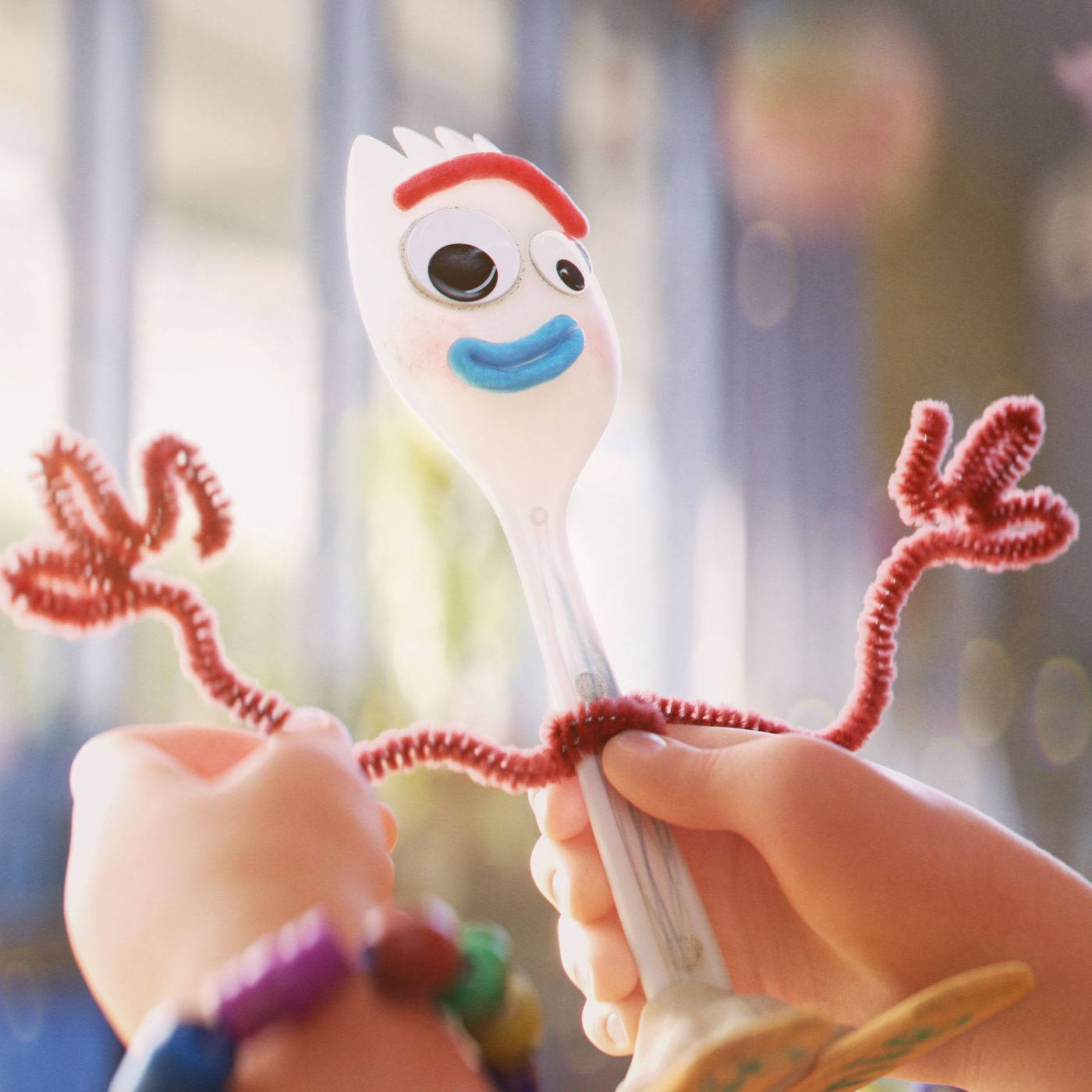 Forky 桌布 壁紙 — 一個快樂的動畫叉子，帶有管道清潔器手臂和藍色微笑，被孩子的手在柔和日光中握住。
