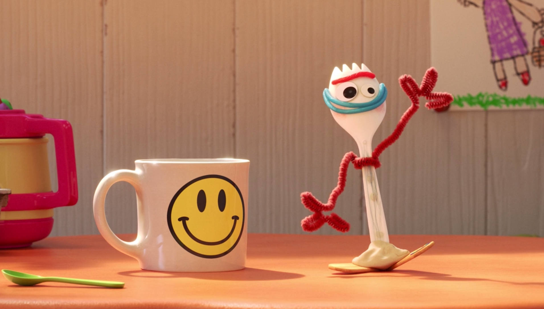 Forky 桌布 壁紙 — 一個快樂的動畫叉子角色，有紅色管道清潔器四肢和藍色頭帶，站在木桌上一個笑臉馬克杯旁邊。