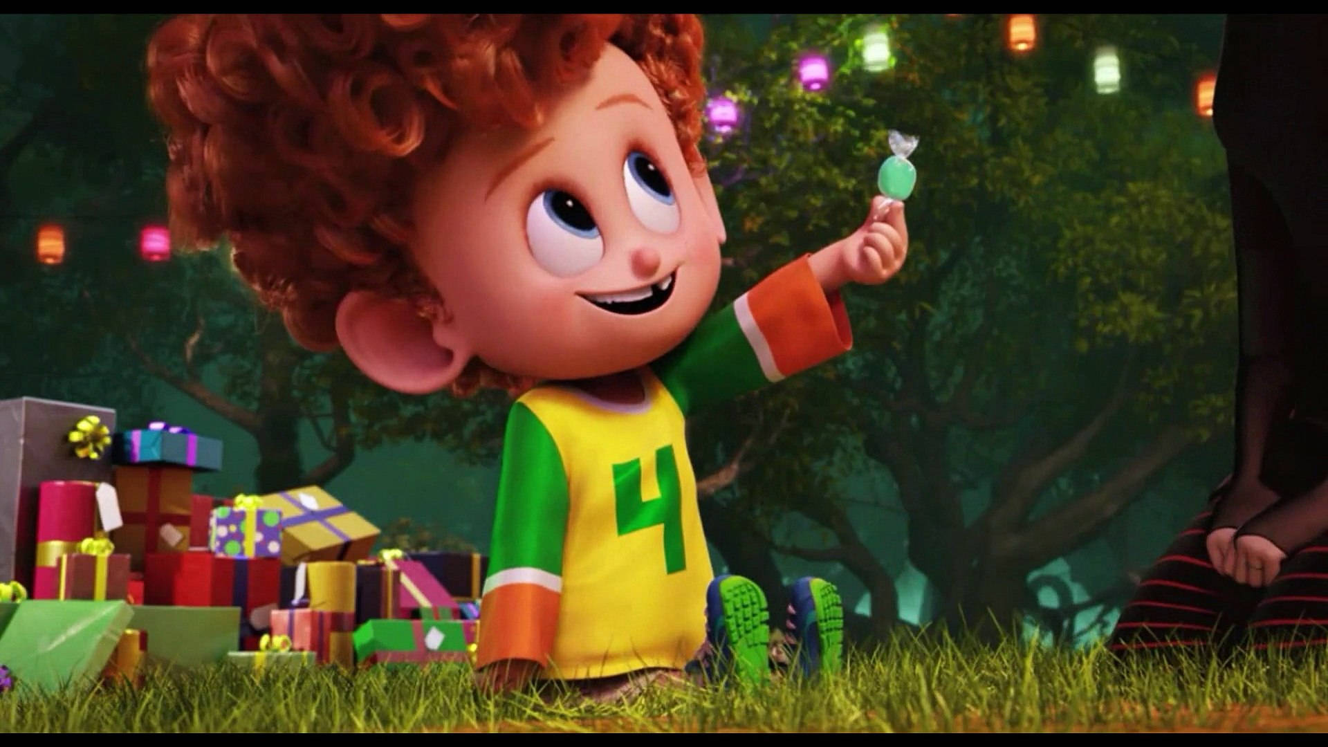 Animated 桌布 壁紙 — 一個快樂的動畫男孩，紅色捲髮，坐在草地上，拿著綠色棒棒糖，周圍是色彩繽紛的禮物，在發光的燈籠下。