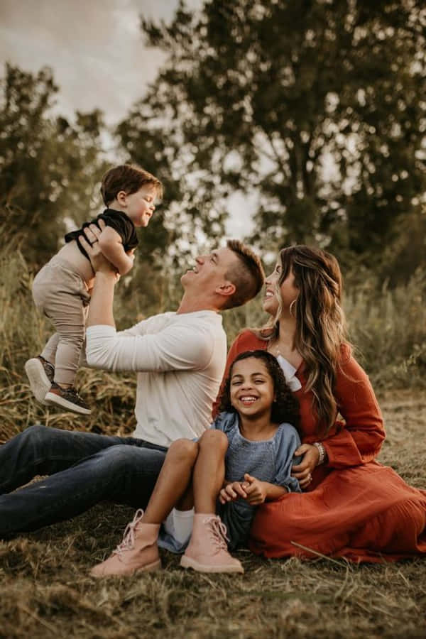 Family 桌布 壁紙 — 一個快樂的四口之家在陽光明媚的田野裡一起大笑，身後有高高的草和樹木。