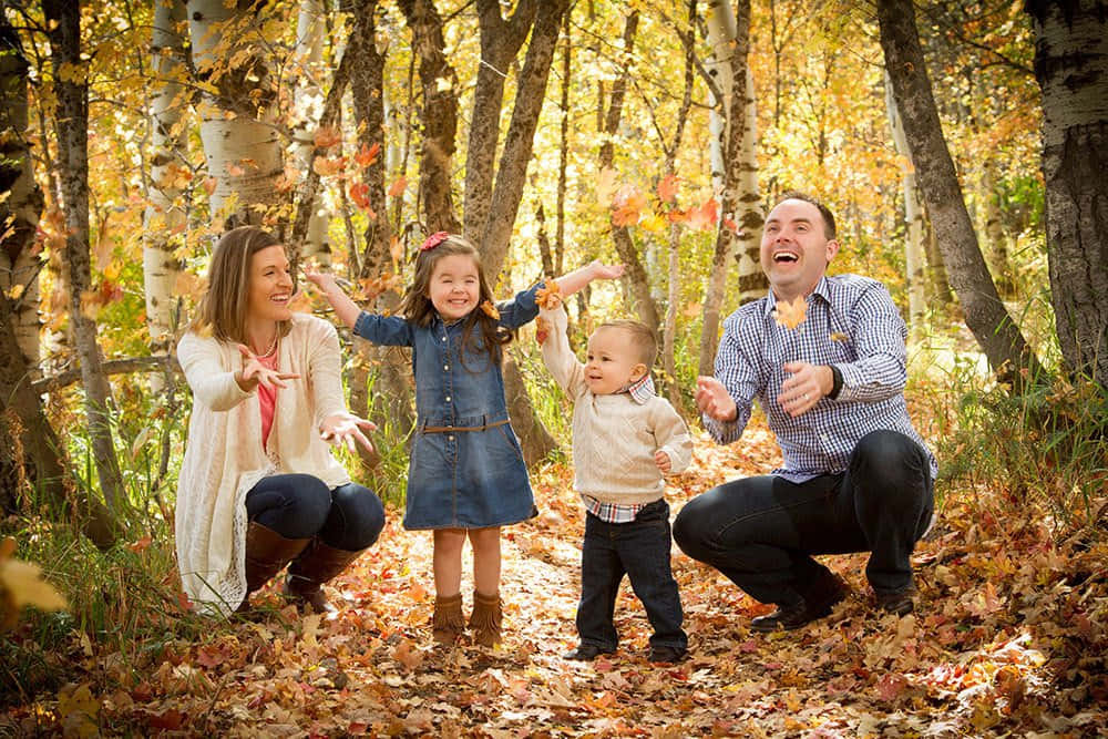 Fall Family 桌布 壁紙 — 一個快樂的四口之家在陽光明媚的白楊林中，笑著拋灑金黃的秋葉。