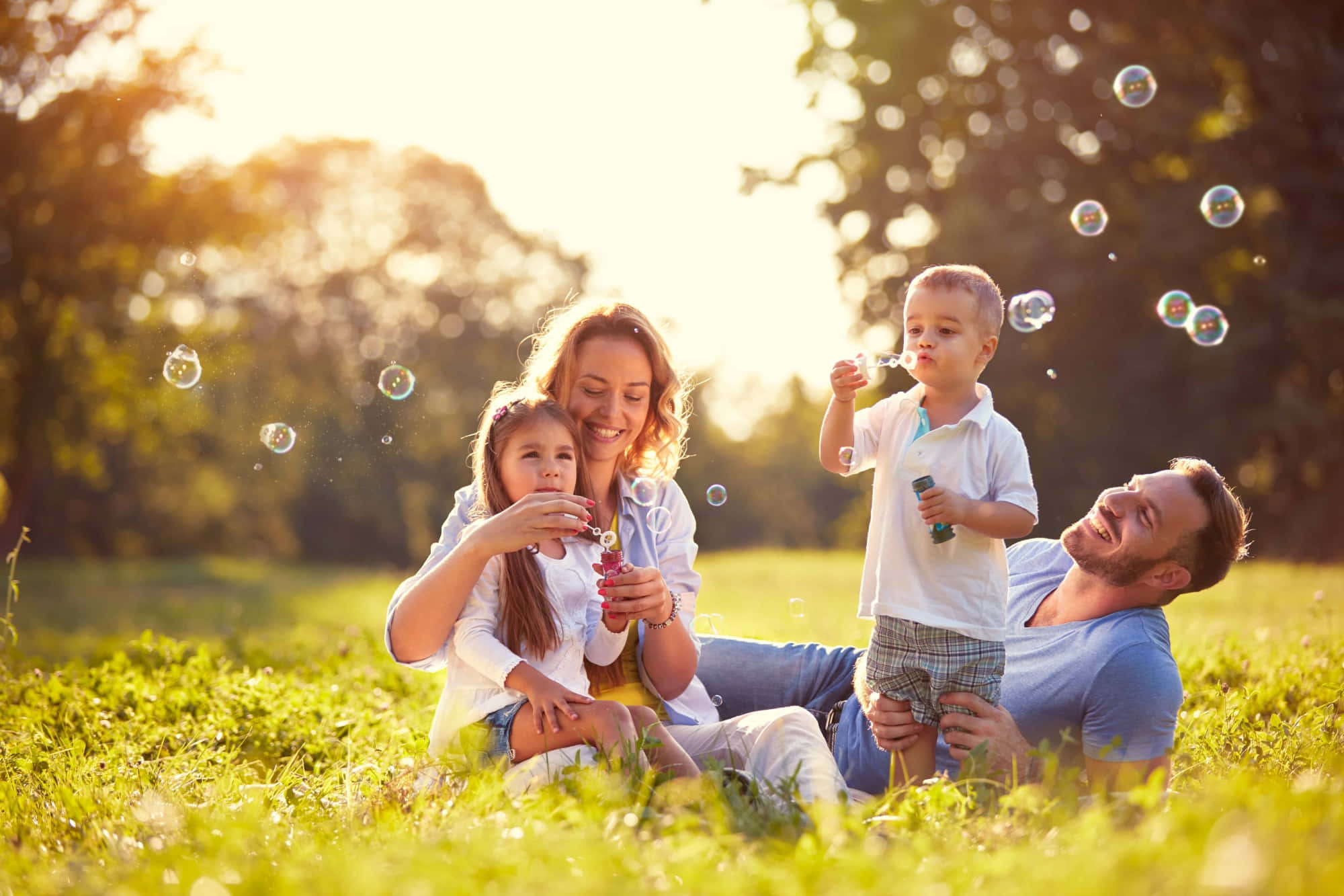 Spring Family 桌布 壁紙 — 一個快樂的四口之家在陽光明媚的草地上一起大笑和吹肥皂泡。