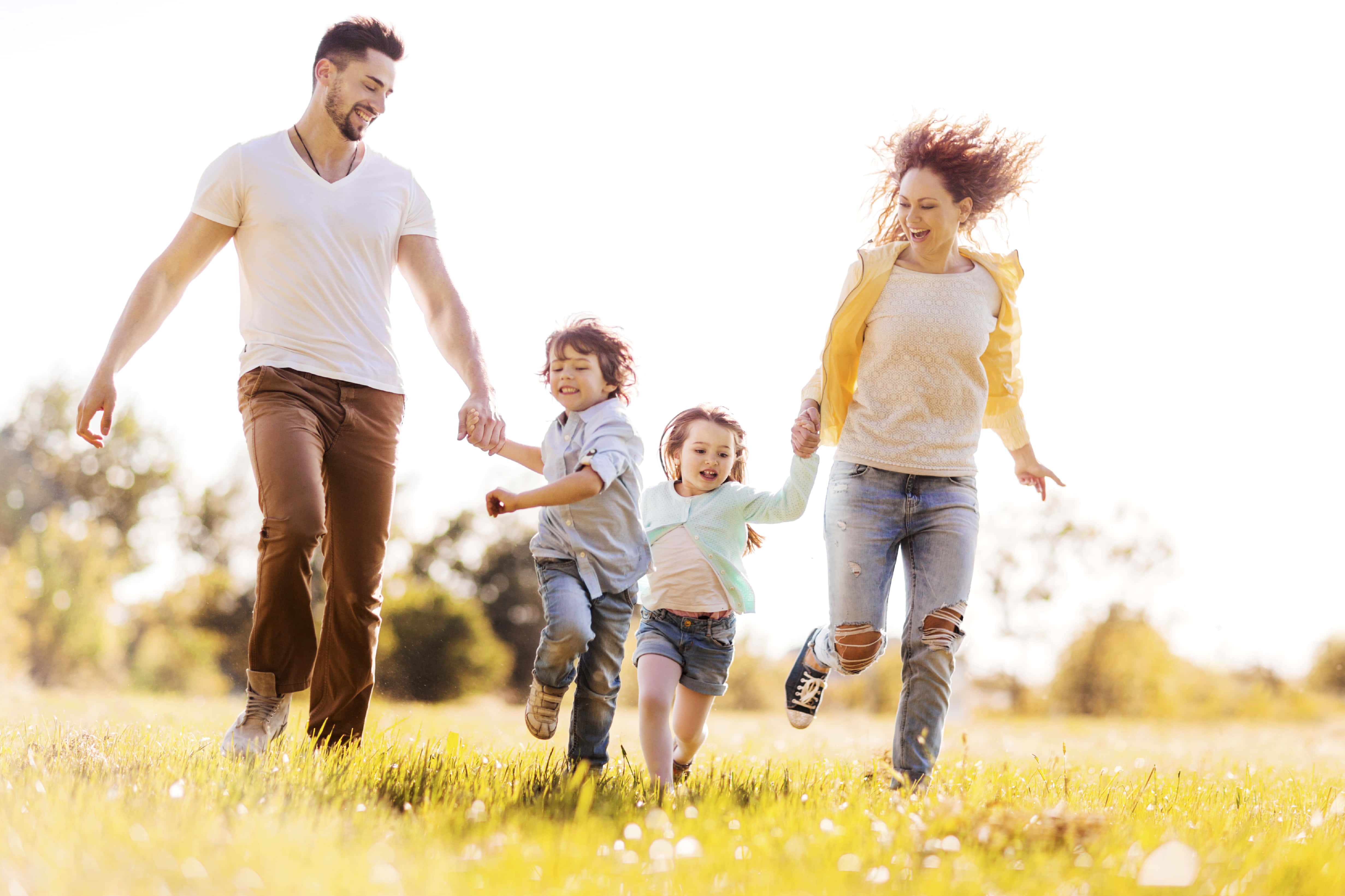 Family 桌布 壁紙 — 一個快樂的四口之家手牽手在陽光明媚的草地上奔跑，頭髮飛揚，笑聲迴盪。