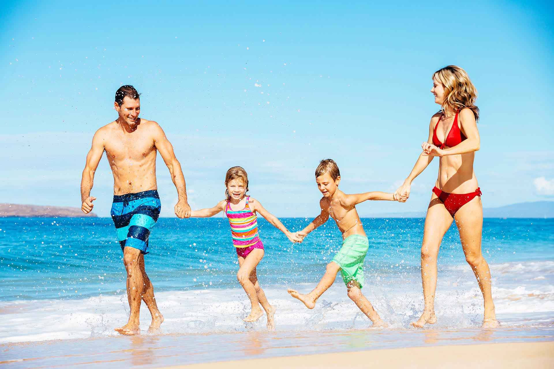 Beach Vacation 桌布 壁紙 — 一個快樂的四口之家手牽手在陽光明媚的海灘上跑過淺淺的海浪。