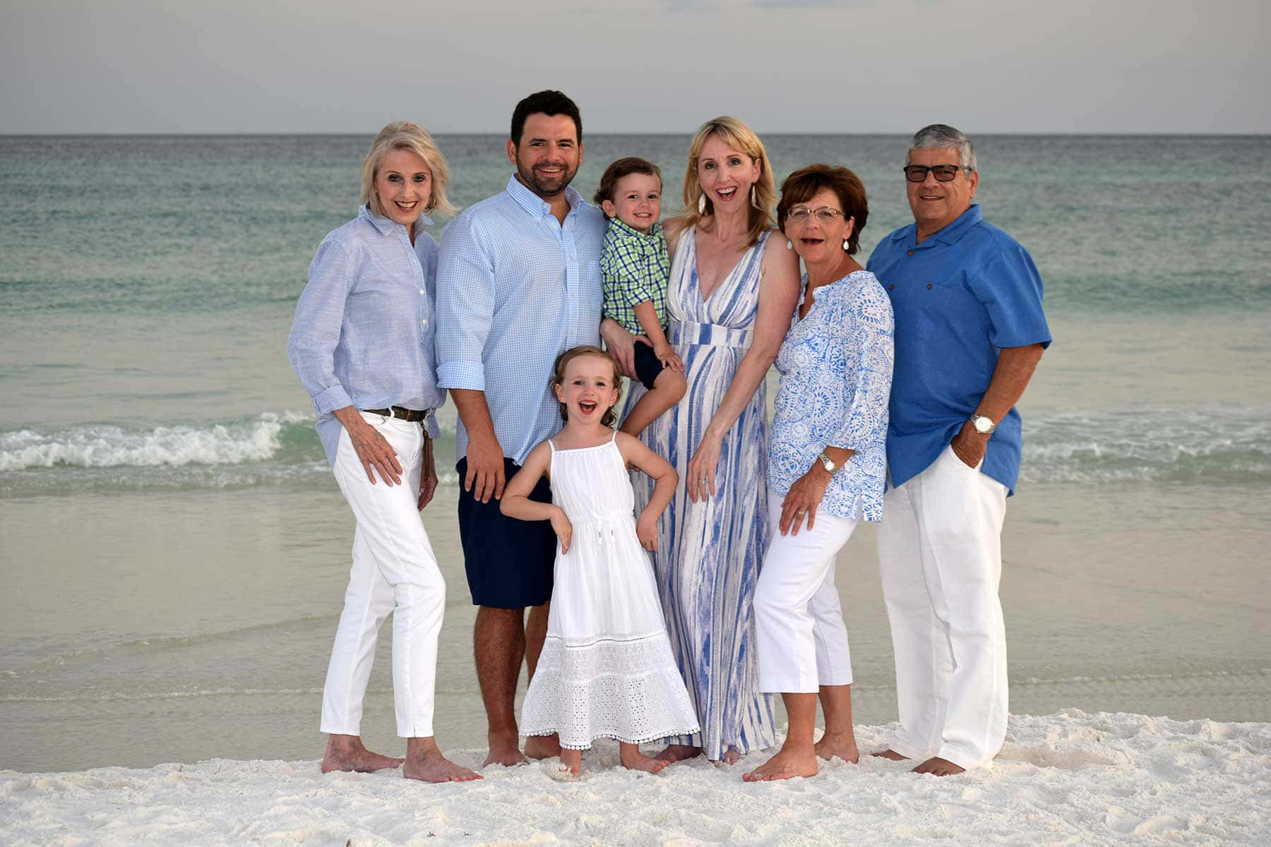 Beach Family 桌布 壁紙 — 一個快樂的多代家庭在陽光明媚的海灘上合影，身後是輕柔的海浪和晴朗的天空。