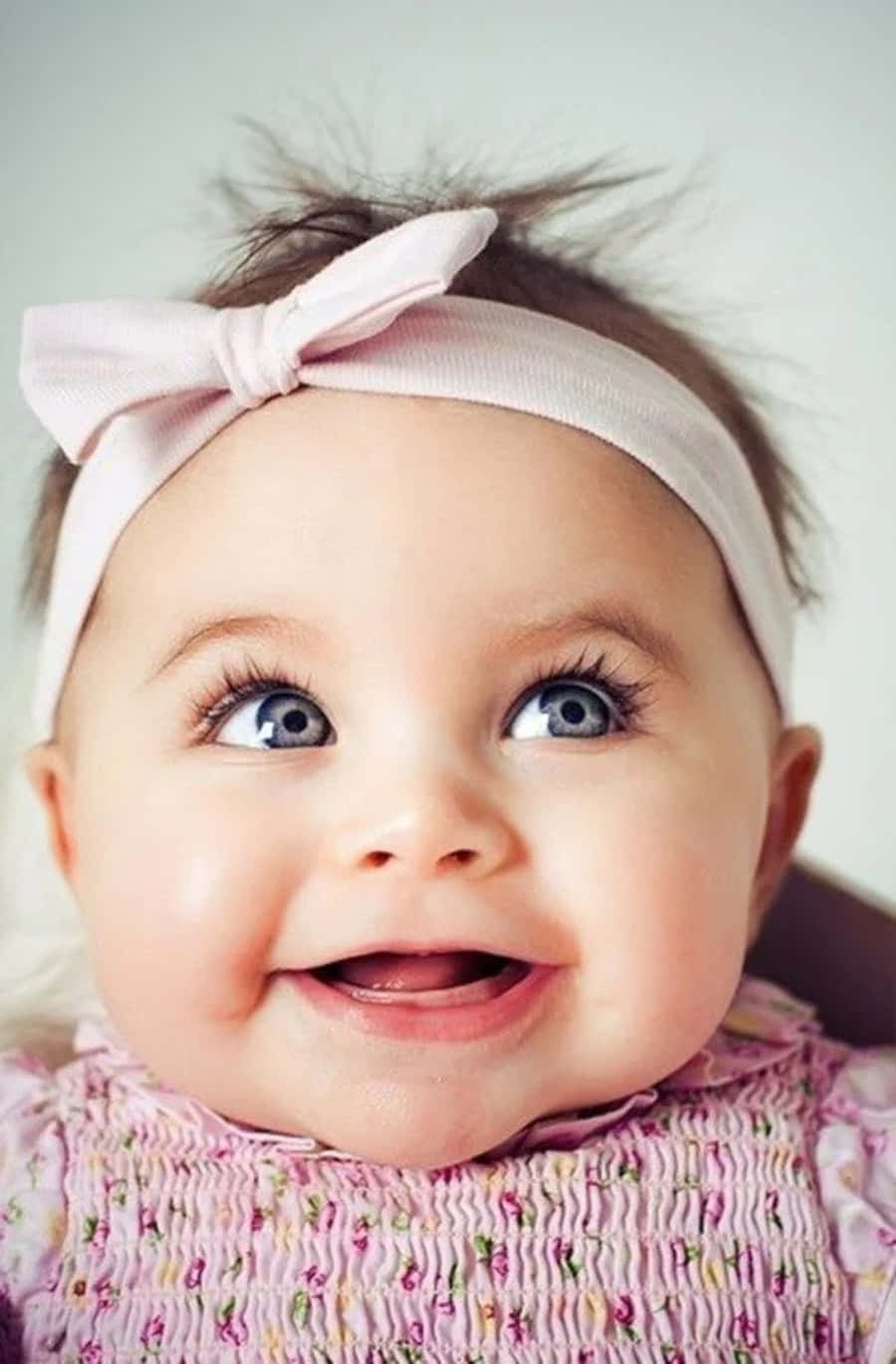 Baby Girl 桌布 壁紙 — 一個快樂的嬰兒，擁有明亮的藍眼睛和粉紅色蝴蝶結頭帶，向上看時露出燦爛的笑容。