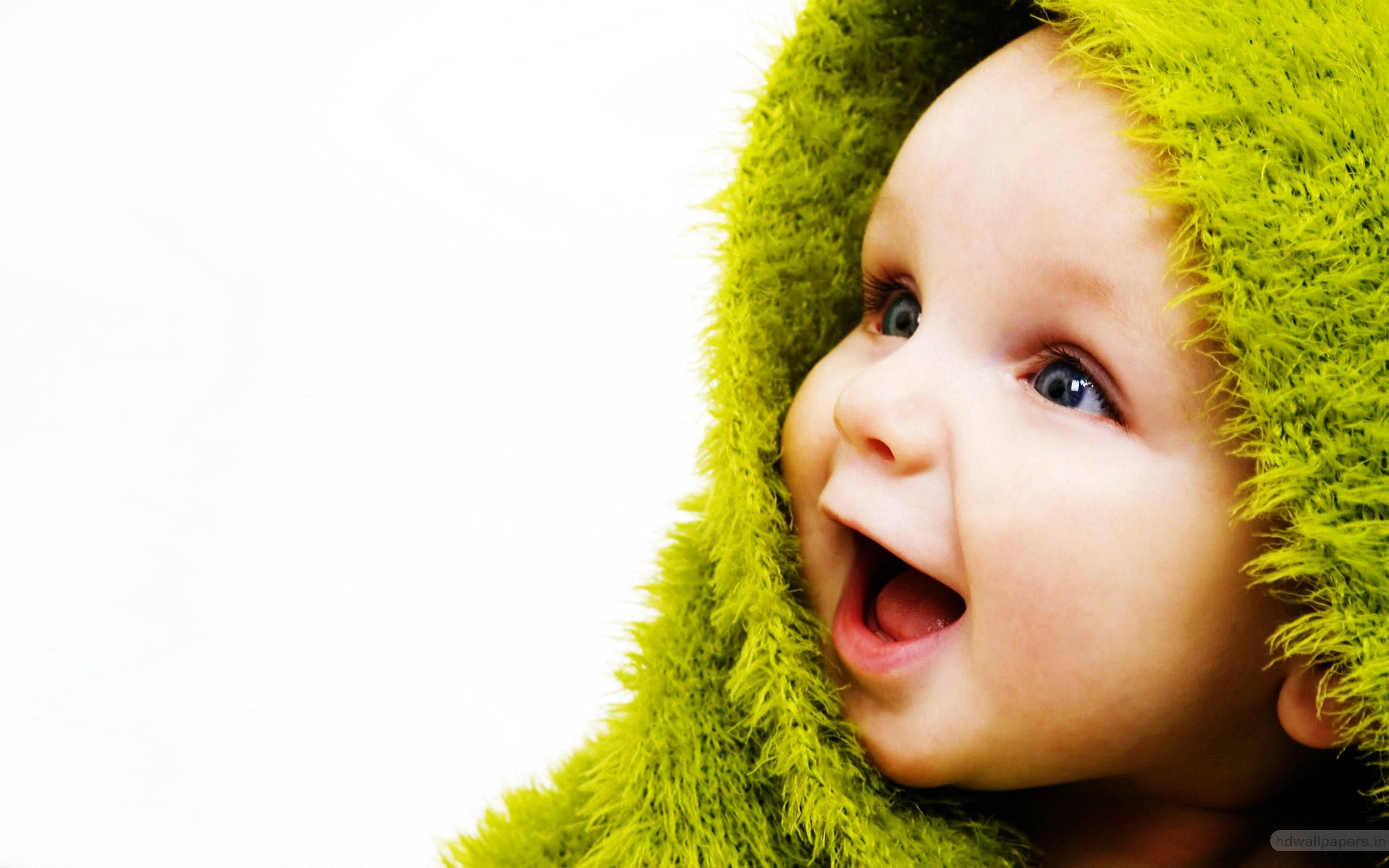 Funny Baby 桌布 壁紙 — 一個快樂的嬰兒，擁有明亮的藍眼睛，在純白背景下戴著毛茸茸的萊姆綠色連帽衫，笑得合不攏嘴。