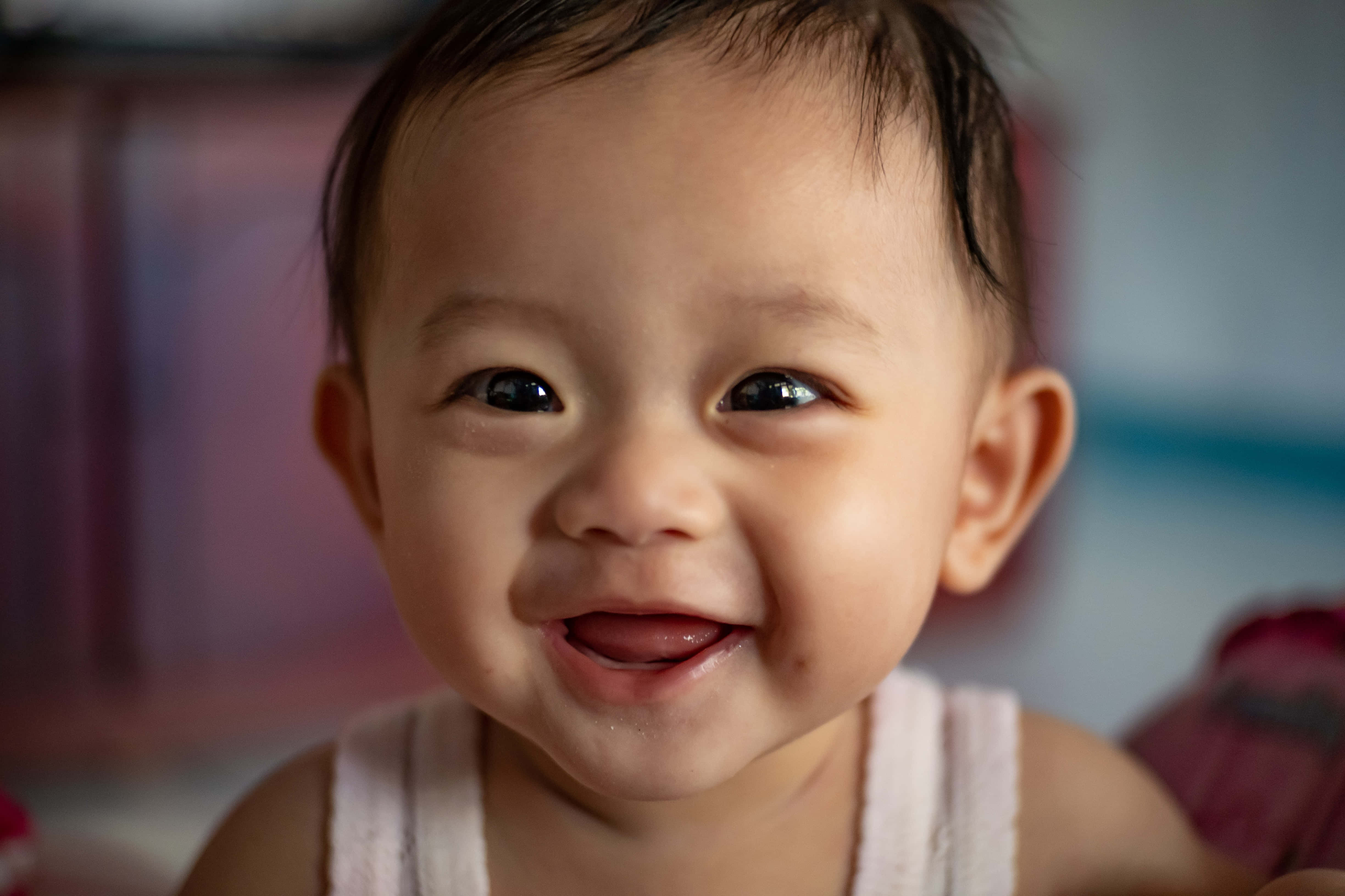 Baby Boy 桌布 壁紙 — 一個快樂的嬰兒，深色眼睛，咧嘴露出無牙的笑容，在柔和自然光下對著鏡頭微笑。