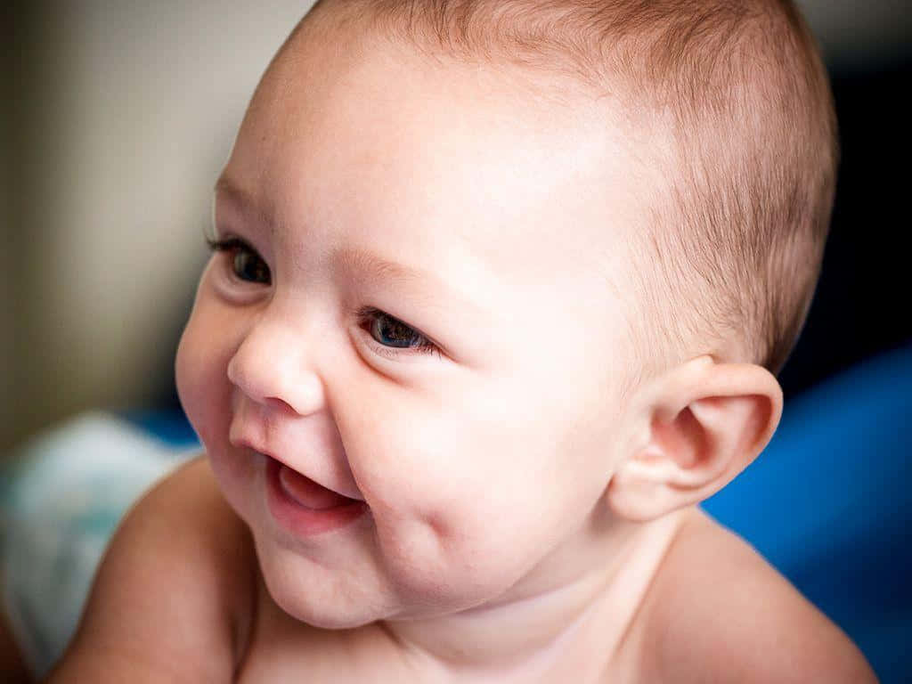 cute baby 桌布 壁紙 — 一個快樂的嬰兒，眼睛明亮，笑容燦爛，在柔和自然光下看向鏡頭外。