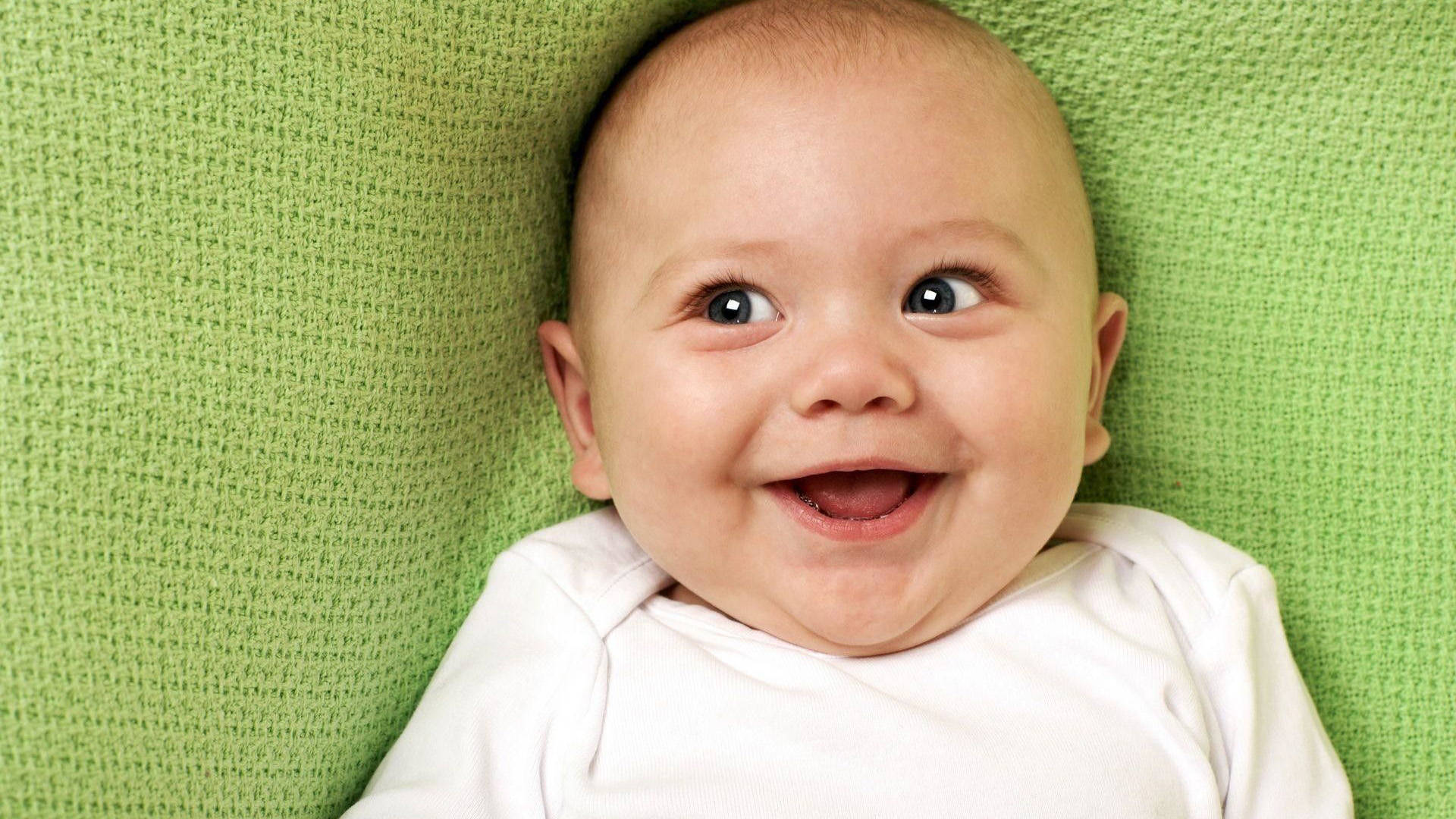faces 桌布 壁紙 — 一個快樂的嬰兒，睜大眼睛，露出燦爛的笑容，躺在有紋理的綠色毯子上。