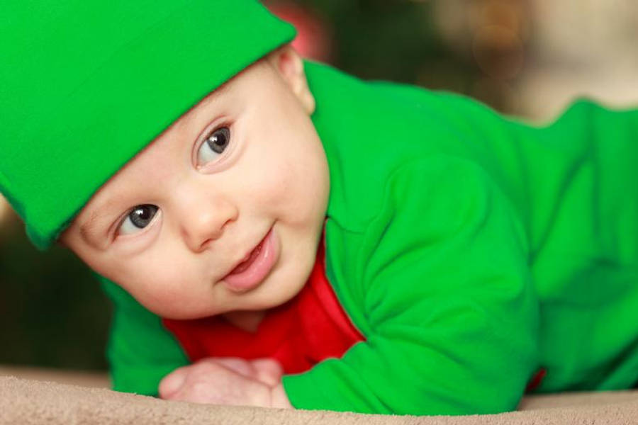 Baby Boy 桌布 壁紙 — 一個快樂的嬰兒穿著鮮綠色精靈服裝，躺在柔軟的地毯上微笑。
