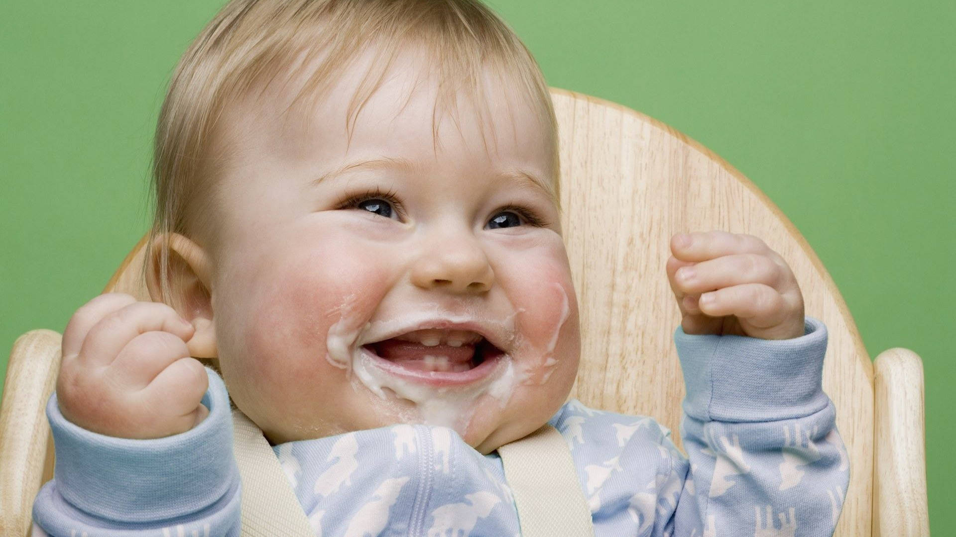 Funny Baby 桌布 壁紙 — 一個快樂的嬰兒臉上沾滿食物，坐在木製高腳椅上，對著綠色背景大笑。